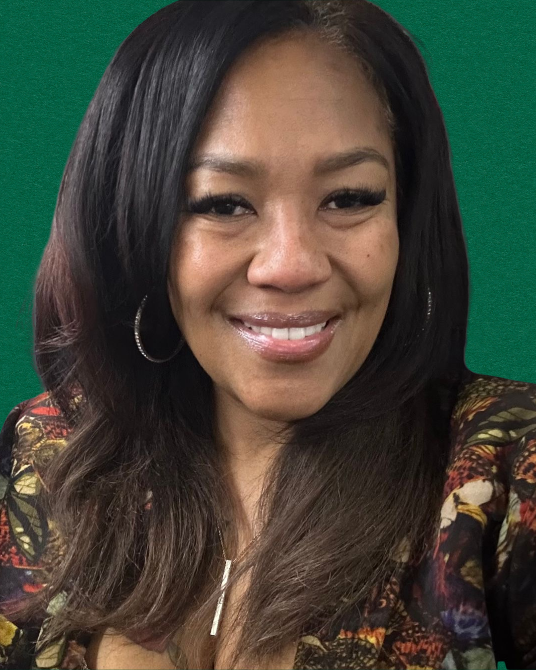 A woman smiling in front of a green background, wearing hoop earrings and a floral-patterned top.
