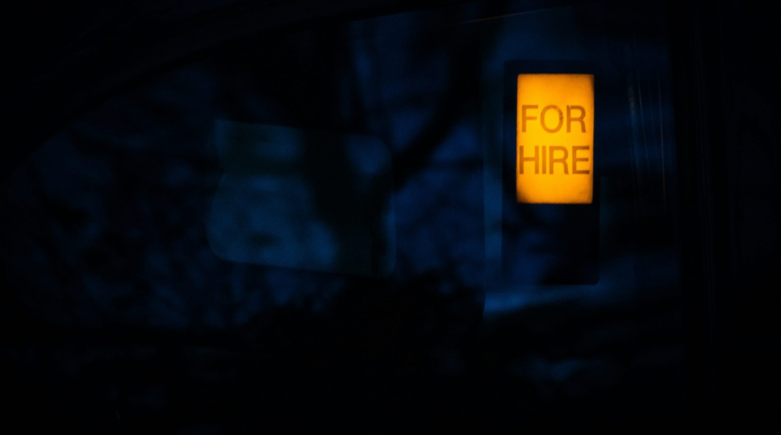 Illuminating "for hire" sign surrounded by darkness