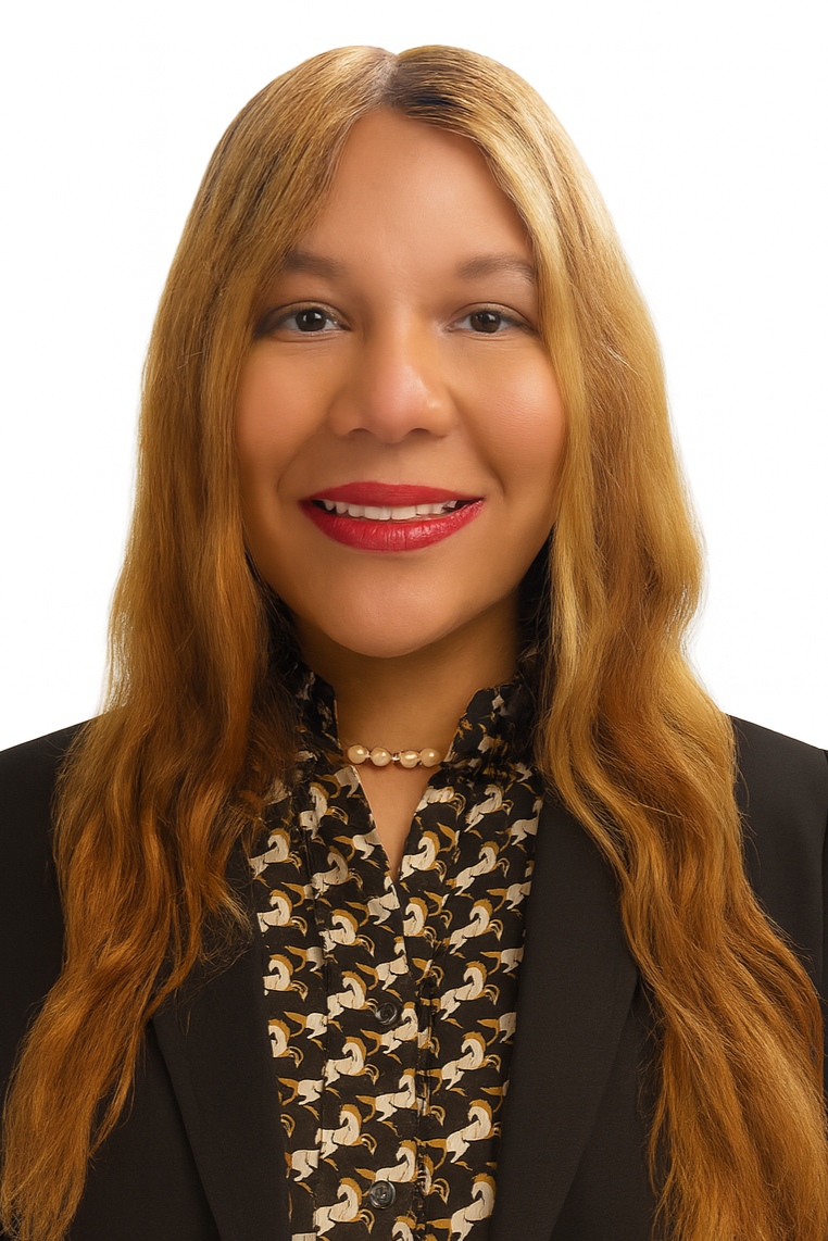 A woman with long red hair, wearing a black blazer and a patterned blouse with a pearl necklace, smiling against a white background.