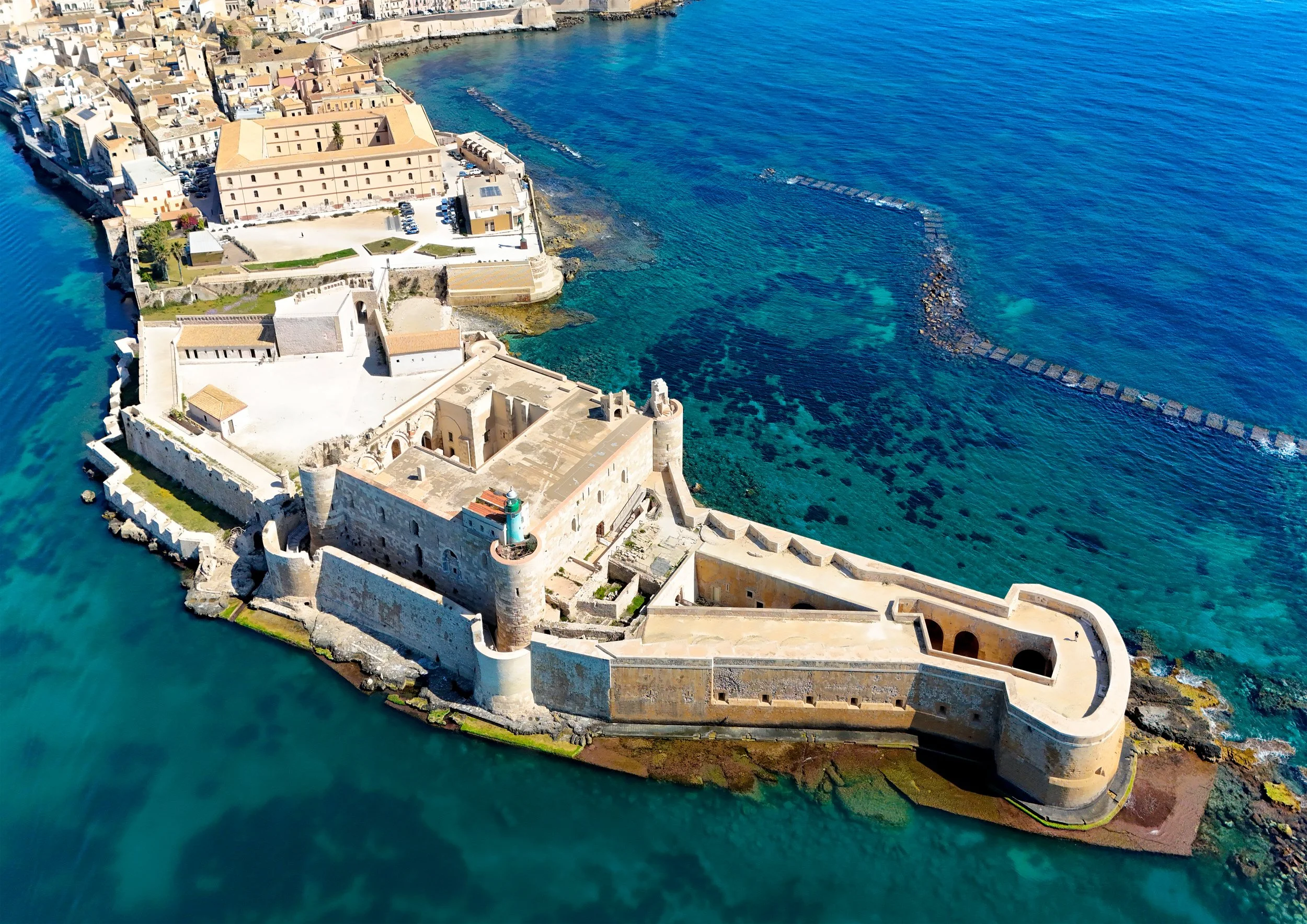 Aerial view of a historic fortress and city on a rocky coastline with clear blue waters.