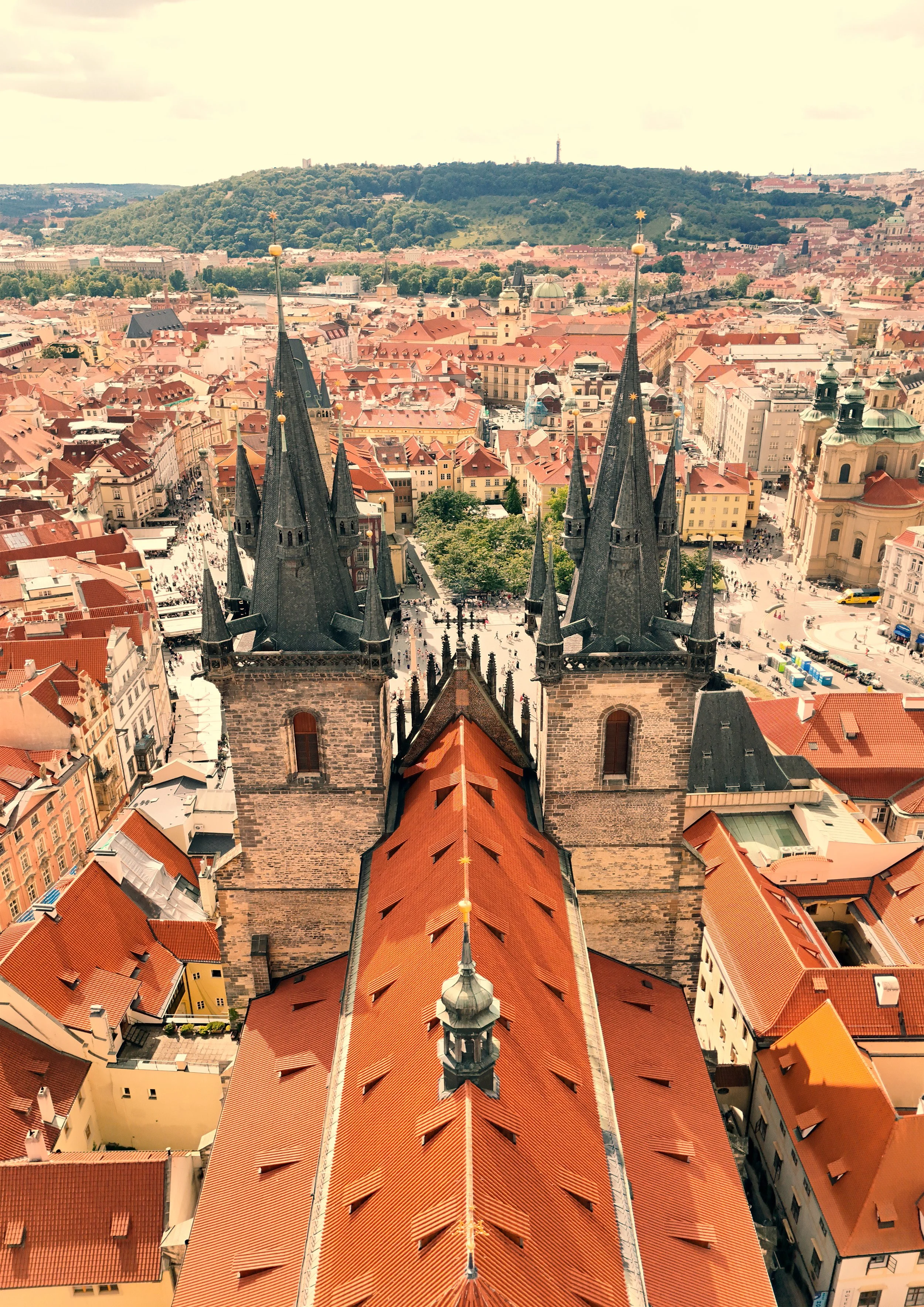 Aerial view of Prague, Czech Republic showing two gothic church spires with red rooftops and a cityscape background.
