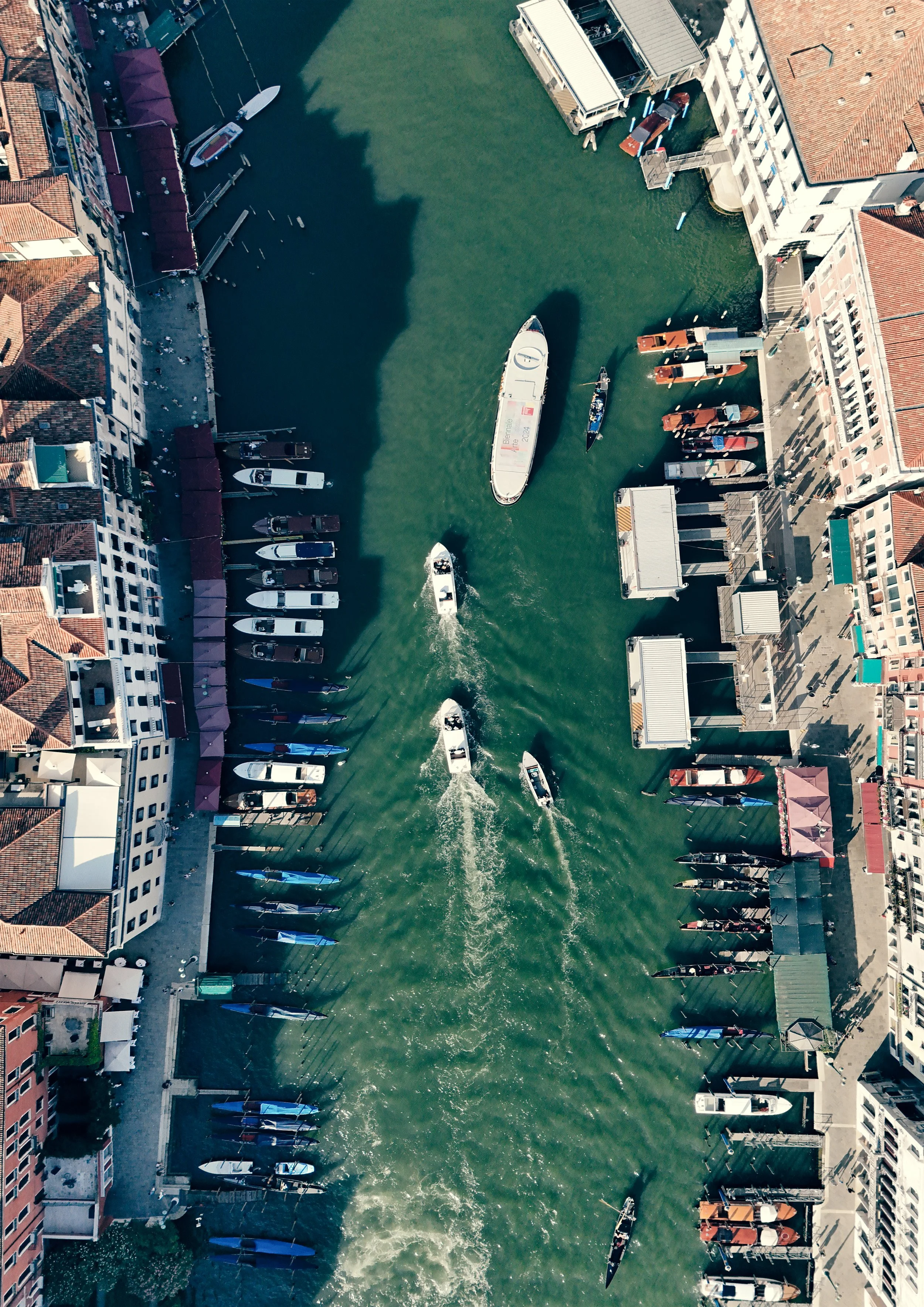 Aerial view of a canal with boats, surrounded by buildings with red-tiled roofs and sidewalks on both sides.