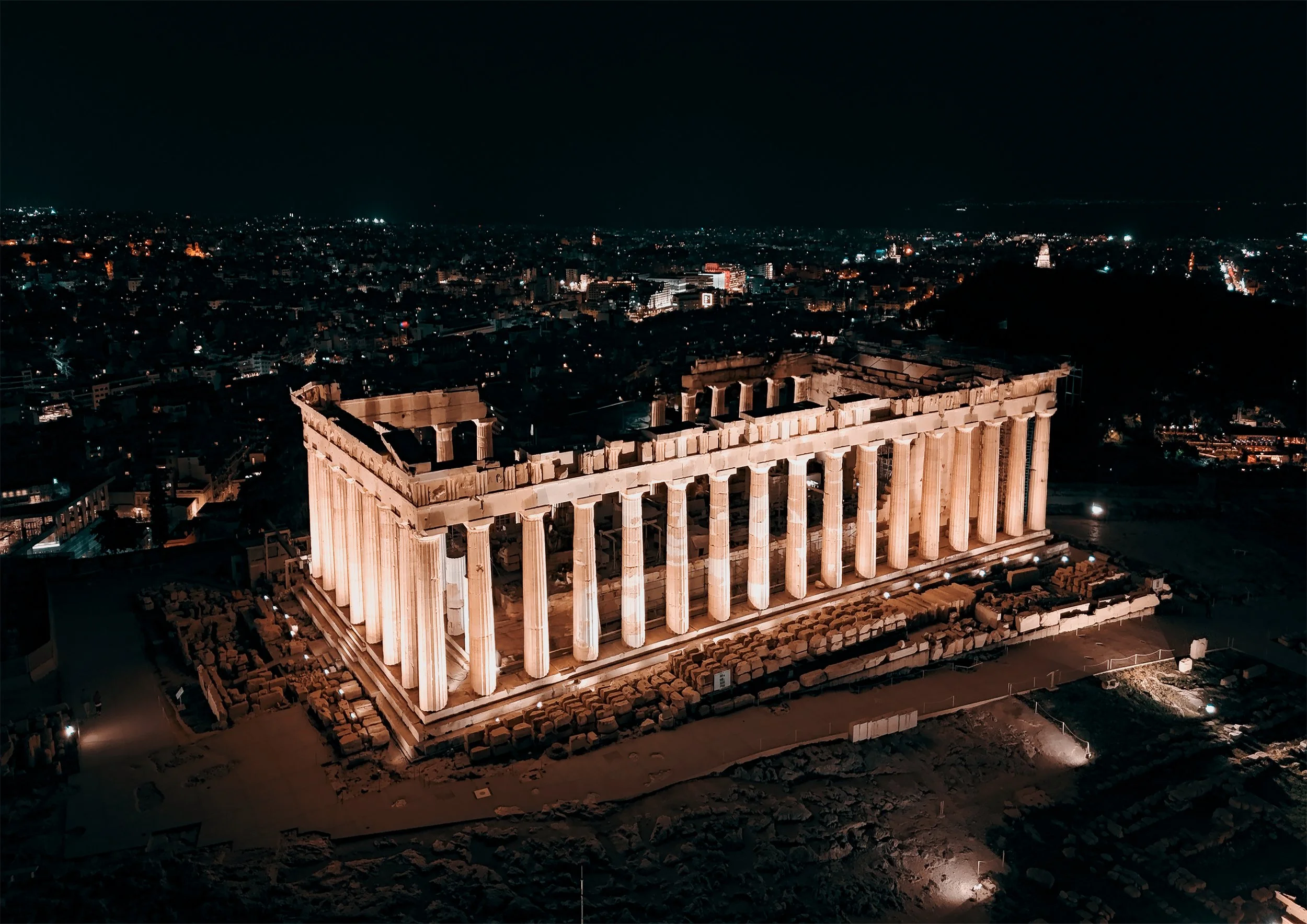 Night view of the illuminated Parthenon temple on Athens Akropolis hillside with city lights in the background.