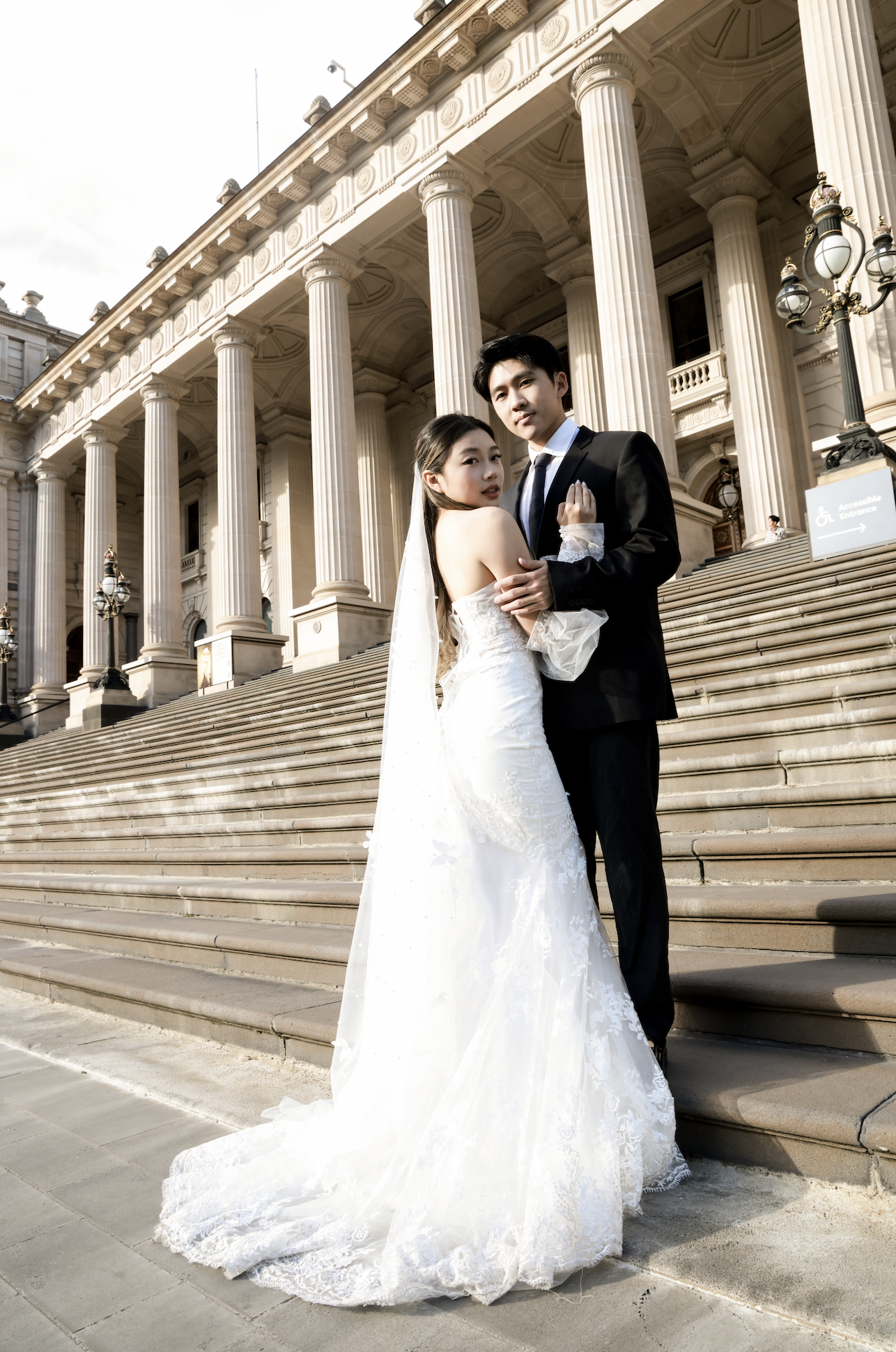 A bride and groom in wedding attire standing on the steps of a classical building with tall columns.