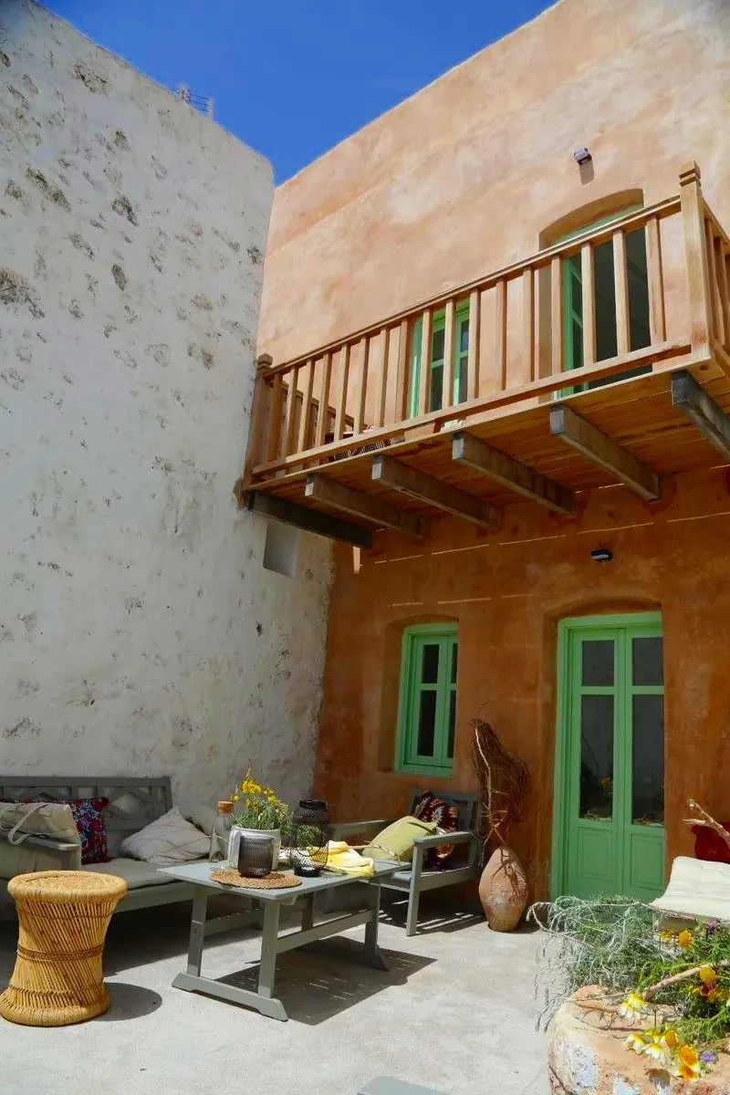 Outdoor patio with a wooden balcony, green window and door frames, and seating area with cushions, plants, and decorative lanterns.
