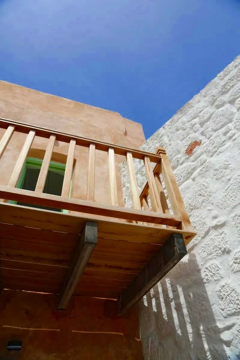 View of a wooden balcony railing and part of the building exterior against a bright blue sky.