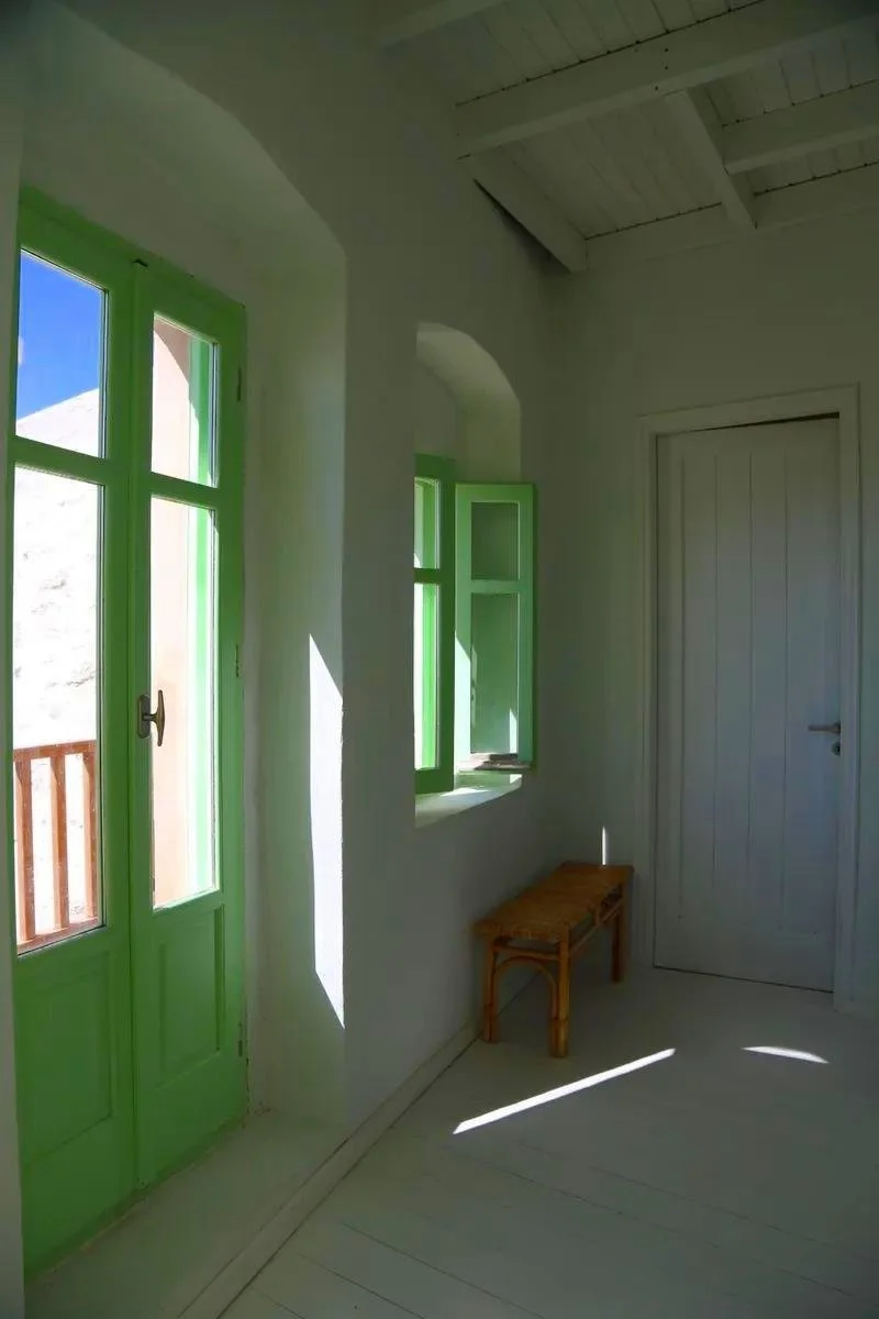 Sunlit room with green window and door frames, wooden bench, white walls and ceiling, and a closed white door.