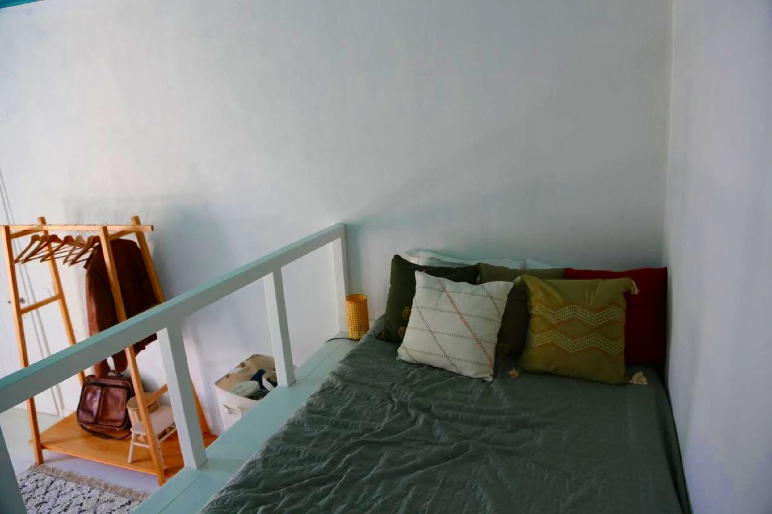 A bed with dark green bedding and multiple decorative pillows in white, green, and red, next to a plain white wall.