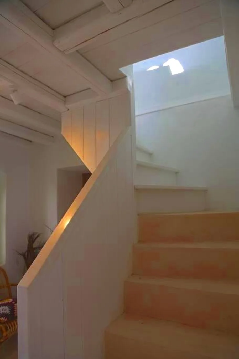 Interior view of a wooden staircase with natural light coming from a skylight or opening at the top.