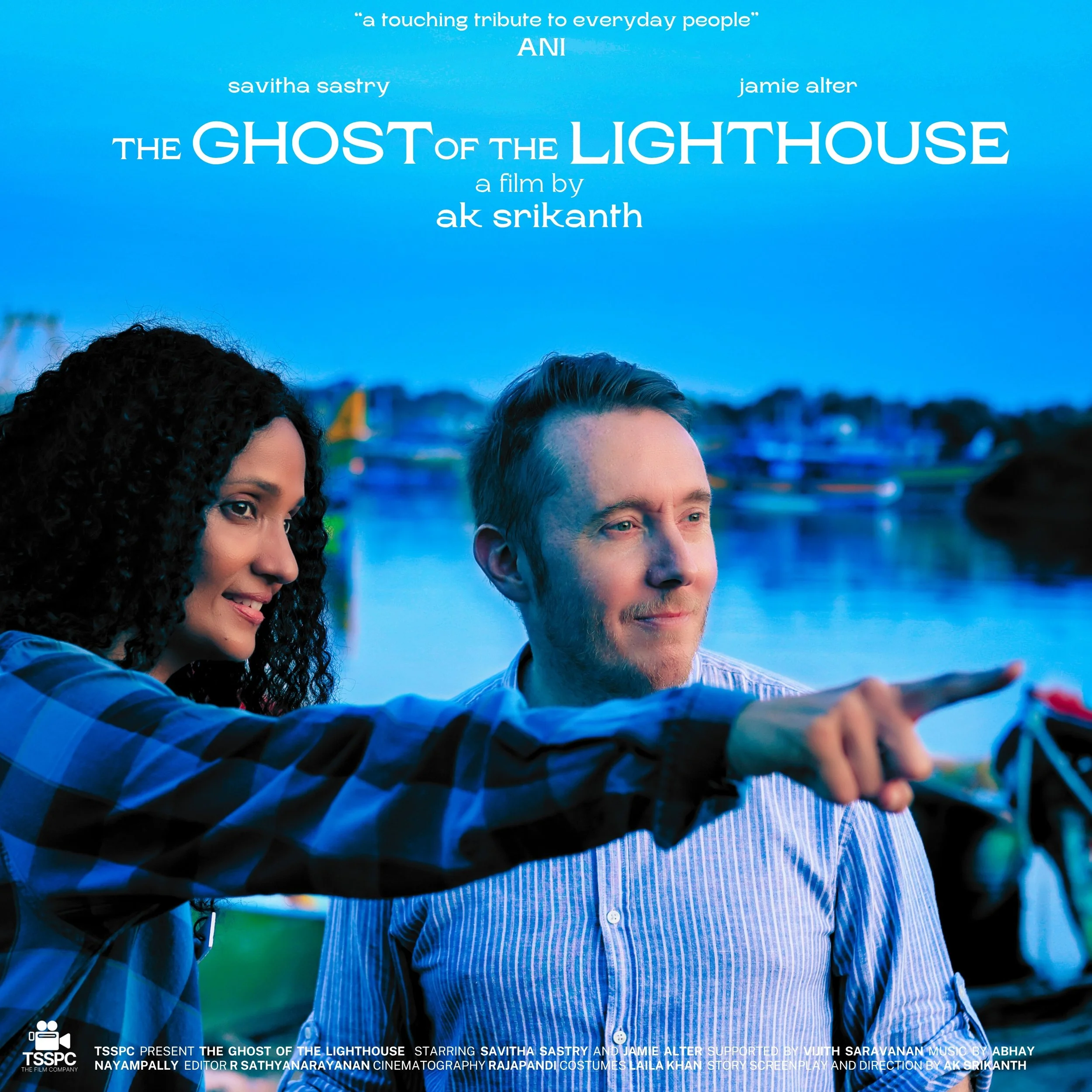 A man and woman standing near a body of water with boats in the background, the woman pointing into the distance. Savitha Sastry and Jamie Alter