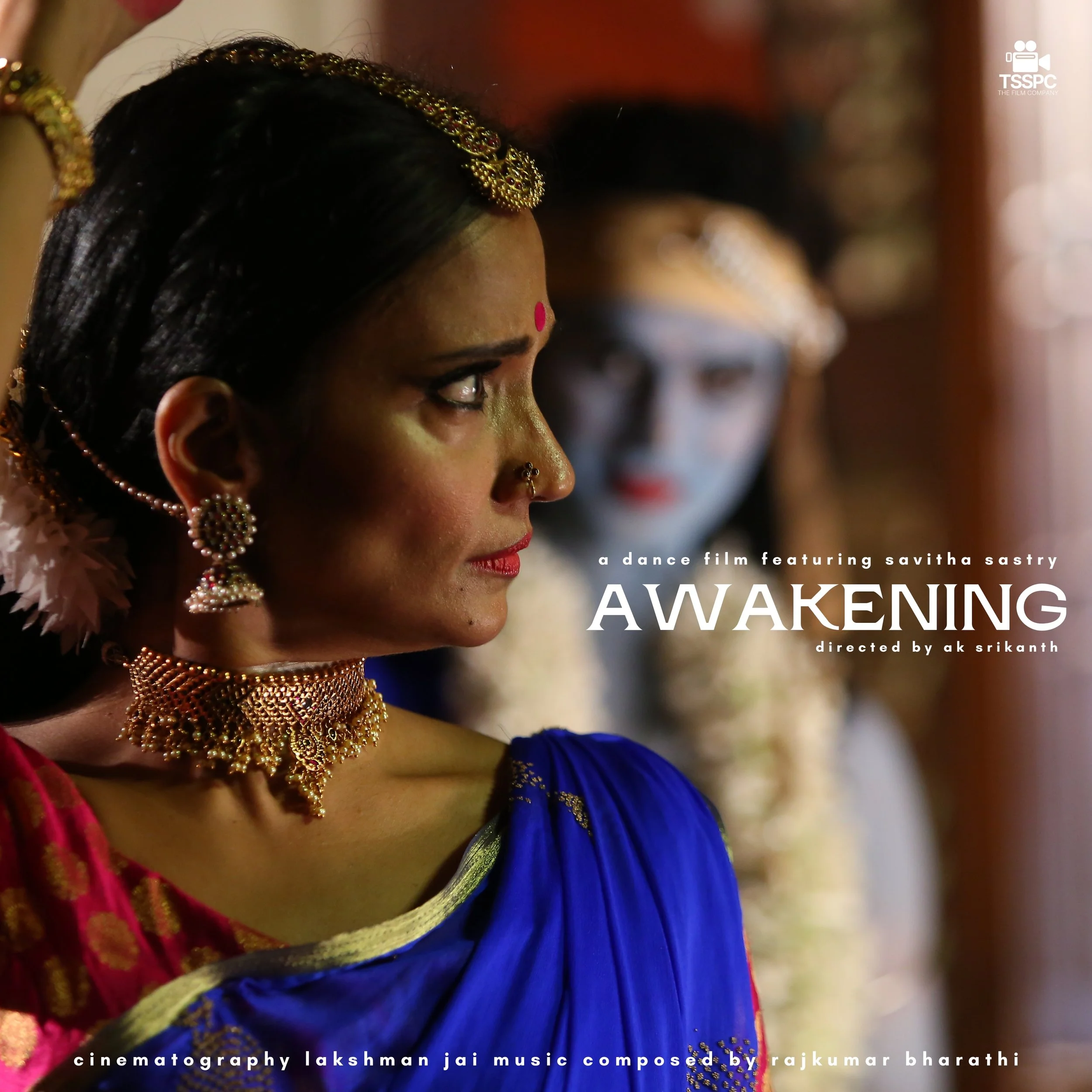 A woman dressed in traditional Indian attire, sitting with her eyes closed and hands resting on her knee, in a warmly lit room.