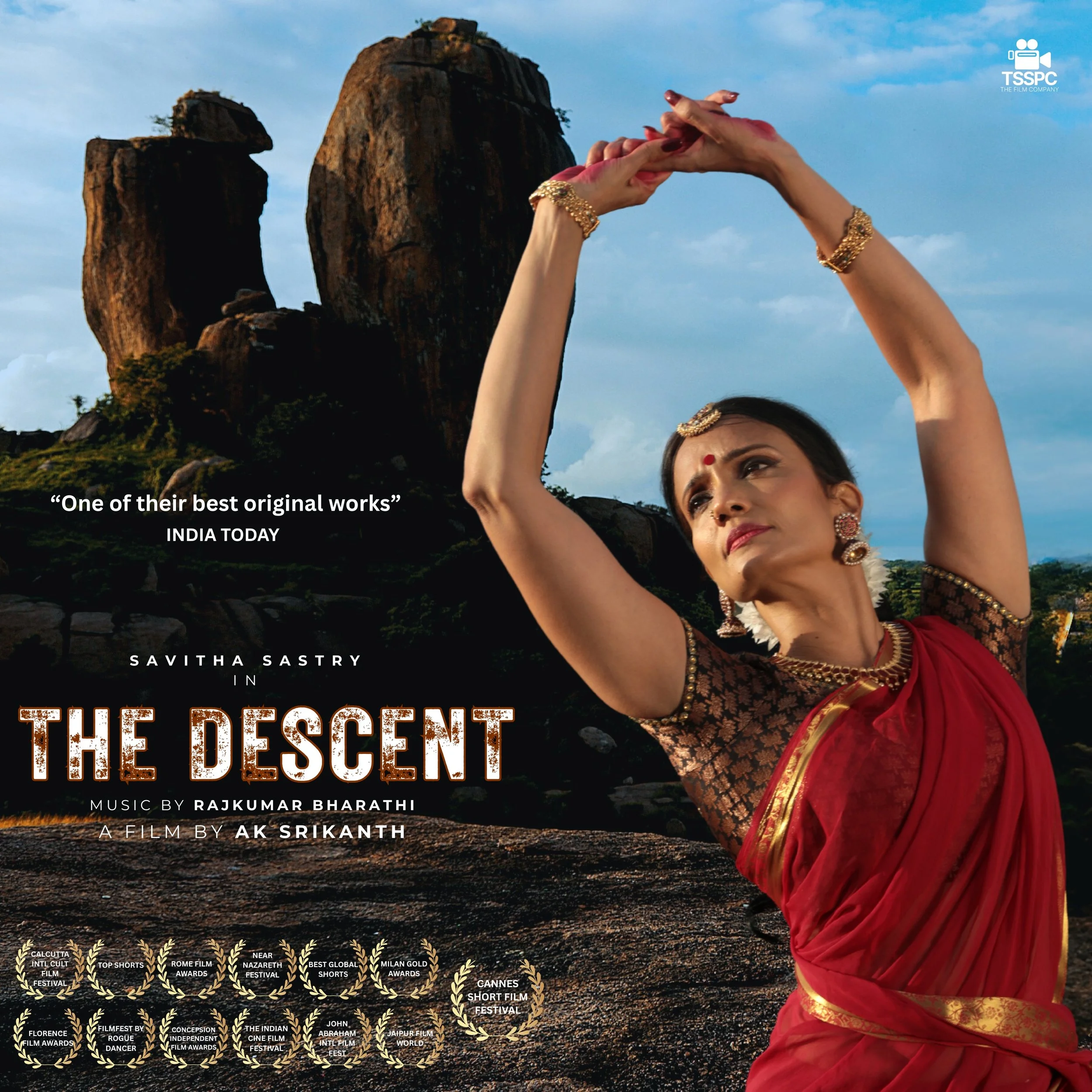 A woman dressed in traditional red Indian attire performing a dance pose on rocky terrain with large rock formations and a cloudy sky in the background. Savitha Sastry Bharatanatyam dance.