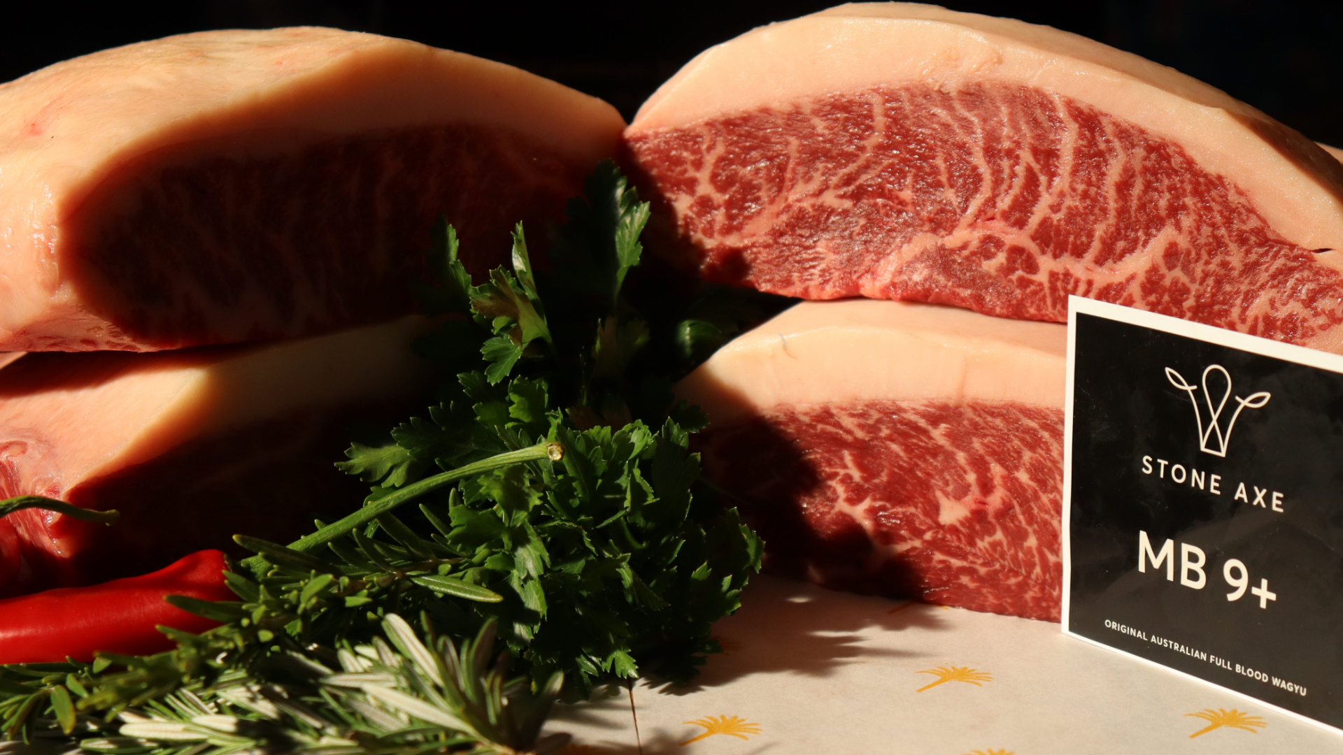 Raw Australian full blood Wagyu beef steaks with fresh herbs and red chili peppers.