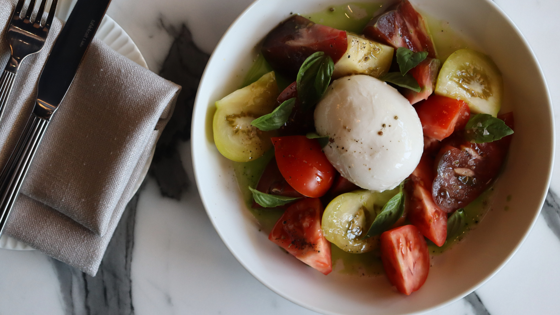 Caprese salad with fresh tomatoes, basil, mozzarella cheese, and olive oil, served in a white bowl on a marble surface.