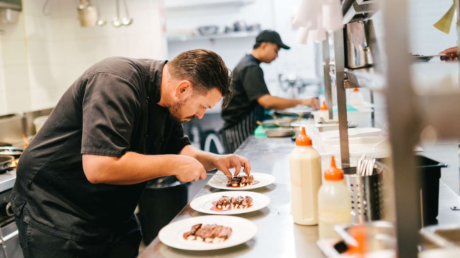 Chef carefully arranges sliced meat on plates in a professional kitchen.