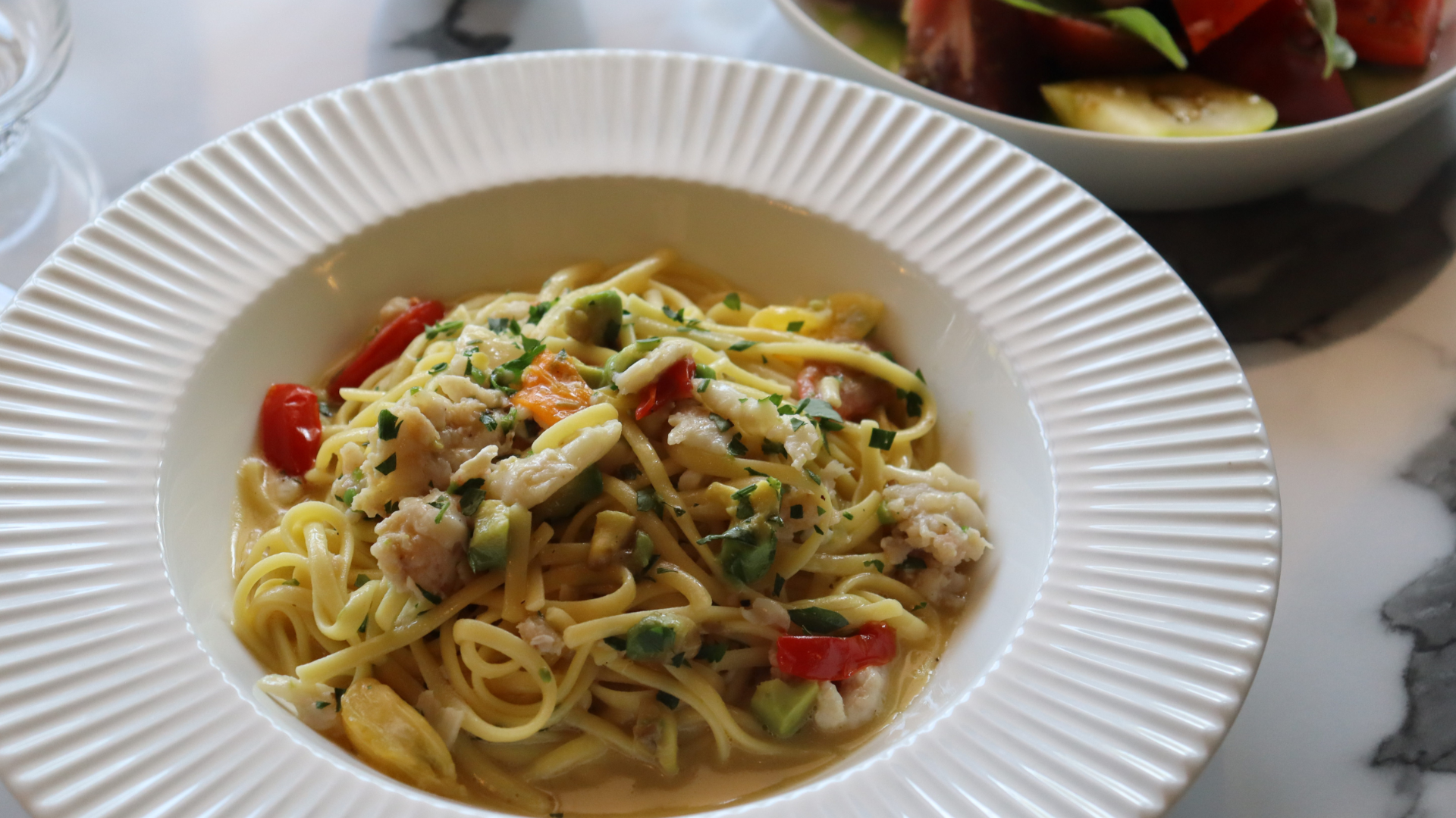 A white bowl of chicken and noodle soup with vegetables and herbs on a marble surface.