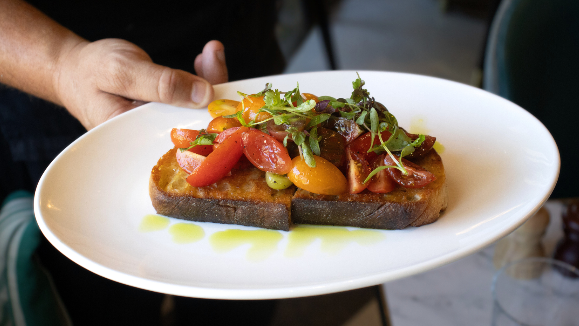 A white plate with a slice of toasted bread topped with chopped cherry tomatoes and microgreens.