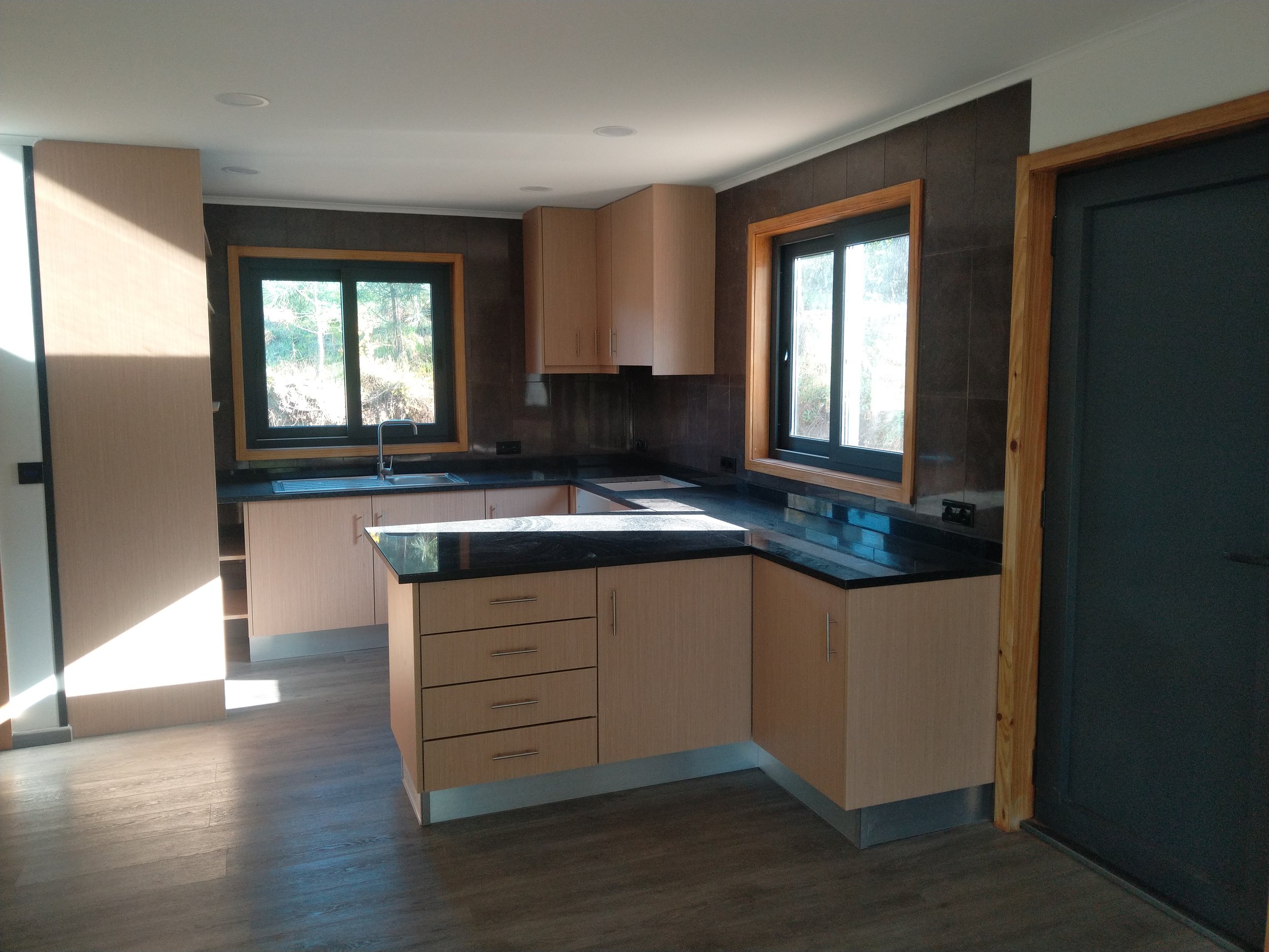 Minimalist room with a small rectangular coffee table casting a shadow on a wooden floor, and a large mirror on the wall reflecting a part of a red pillow.