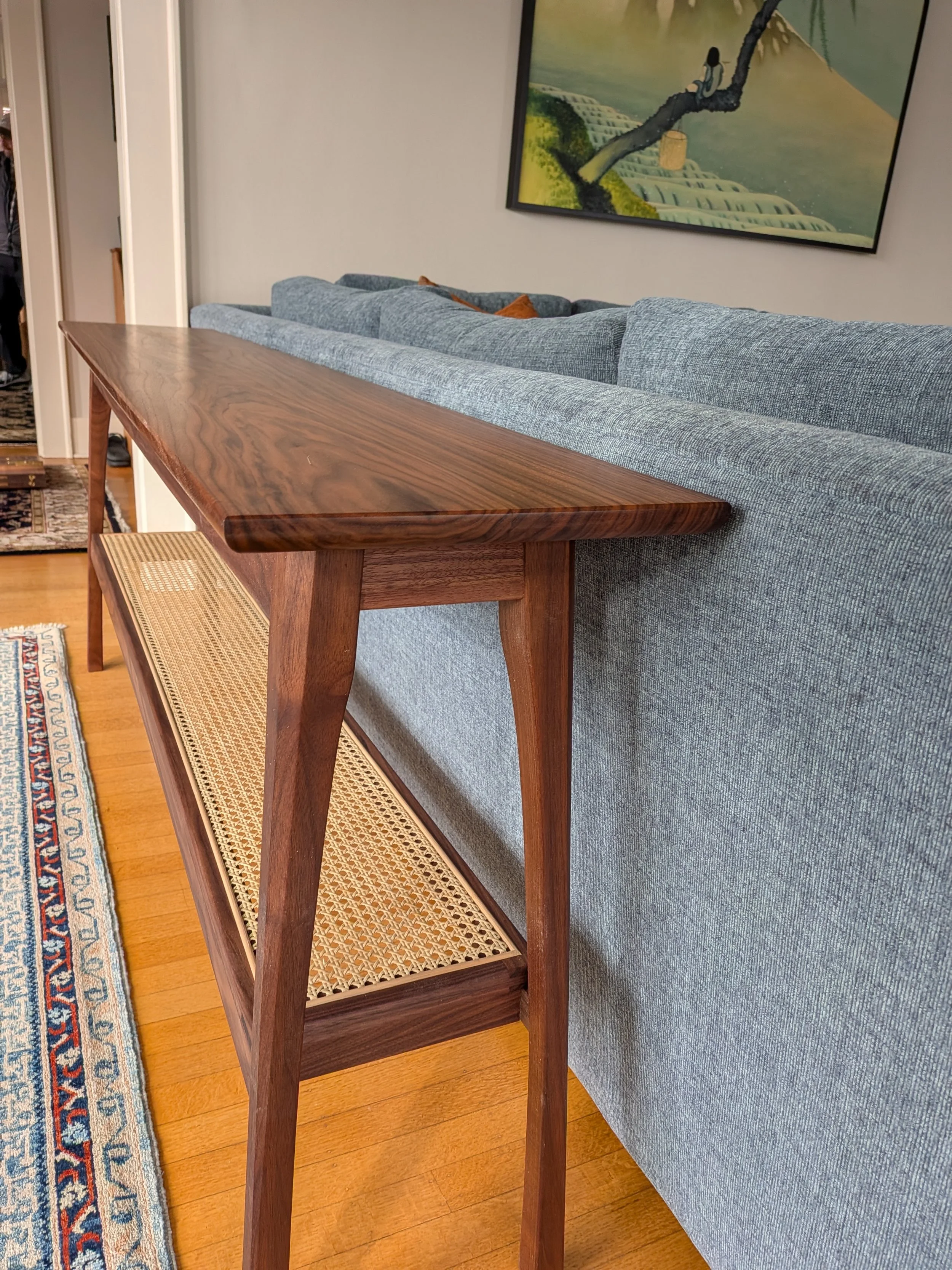 Walnut sofa table detail showing splayed legs, curved aprons, and cane shelf