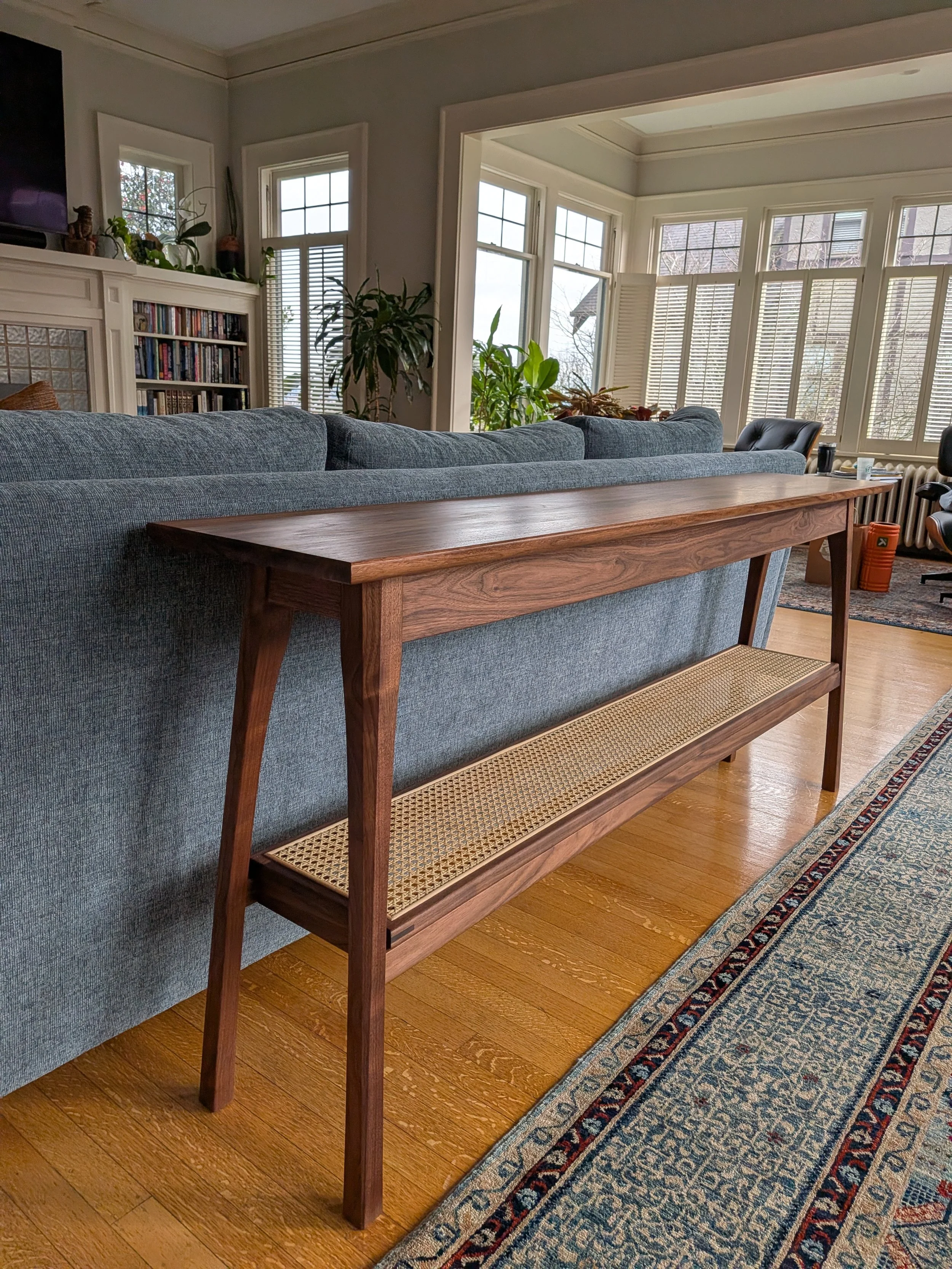 Handcrafted walnut console table with open-weave cane lower shelf, side view