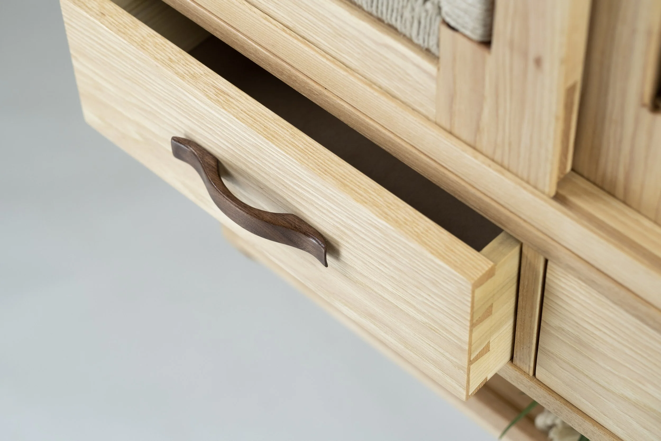 Close-up of a wooden drawer with a curved dark wood handle, partially open.