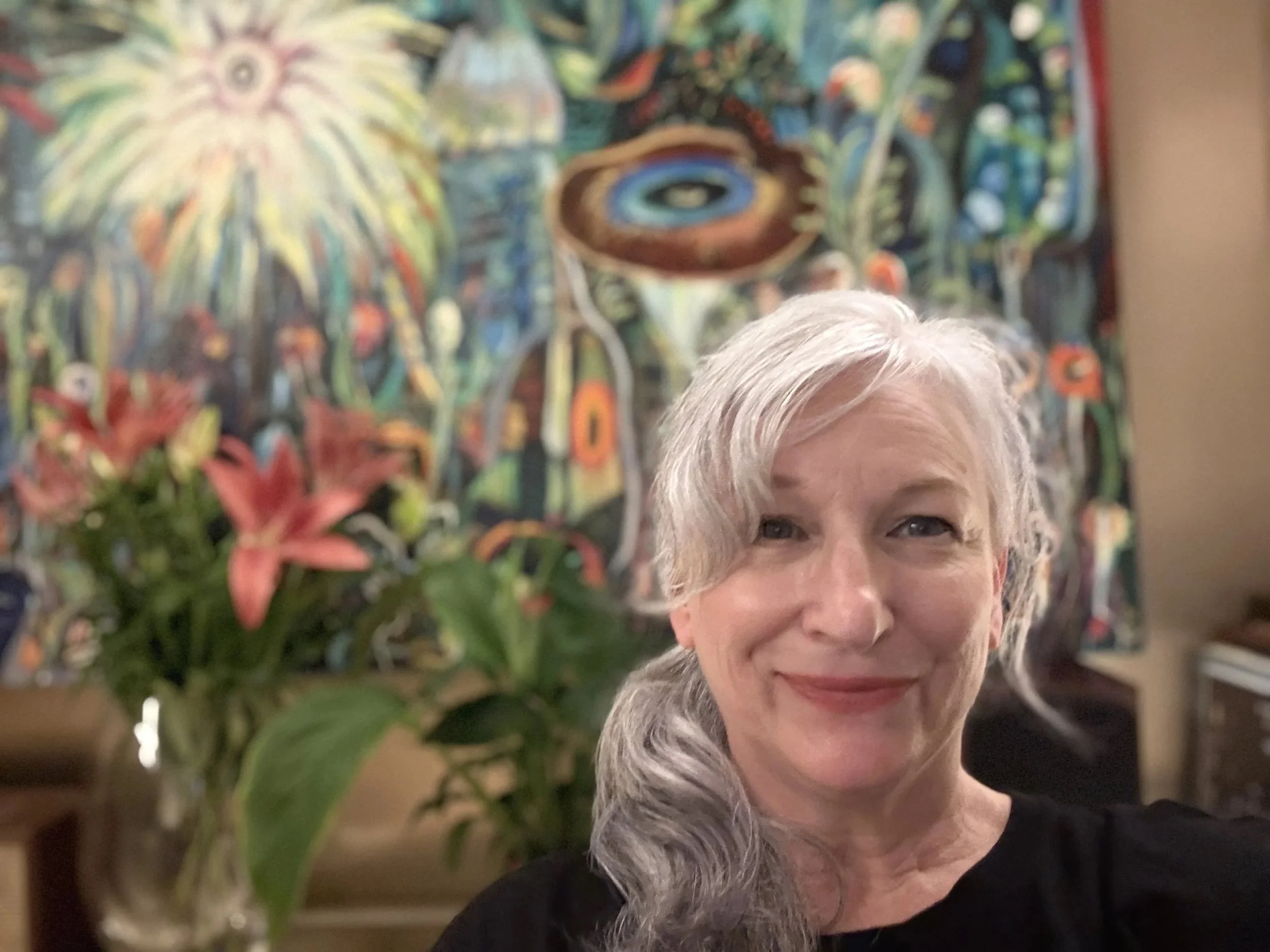 Hilary Lee smiling in front of colorful abstract artwork and a vase of pink lilies.