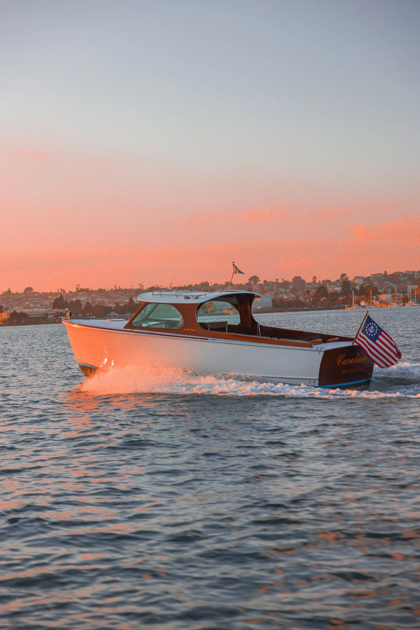 A boat moving on the water during sunset with an American flag at the stern and a distant shoreline in the background.