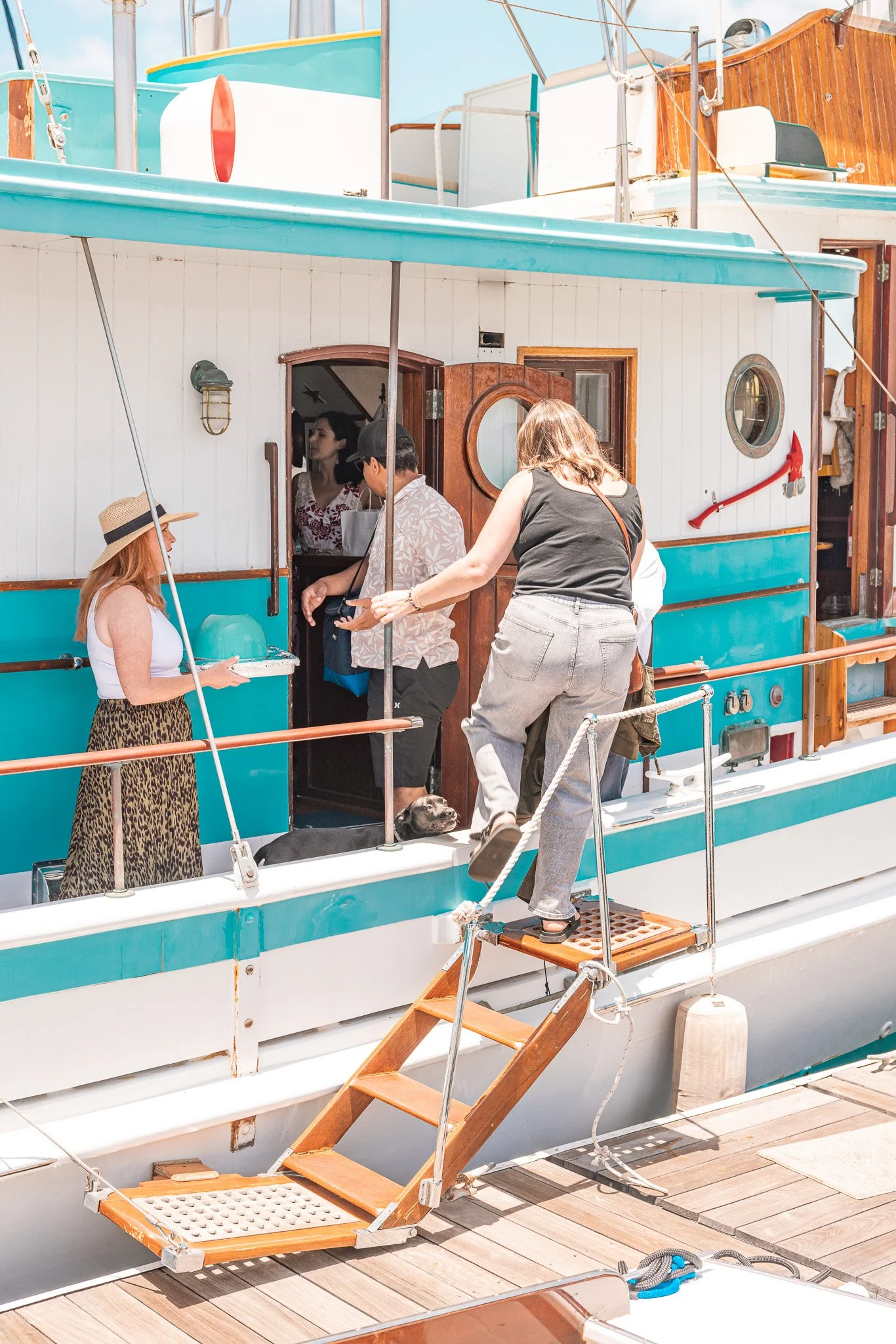 People disembarking from a boat docked at a wooden pier, with some on the boat and one woman on the gangway, engaging with the crew at the entrance.