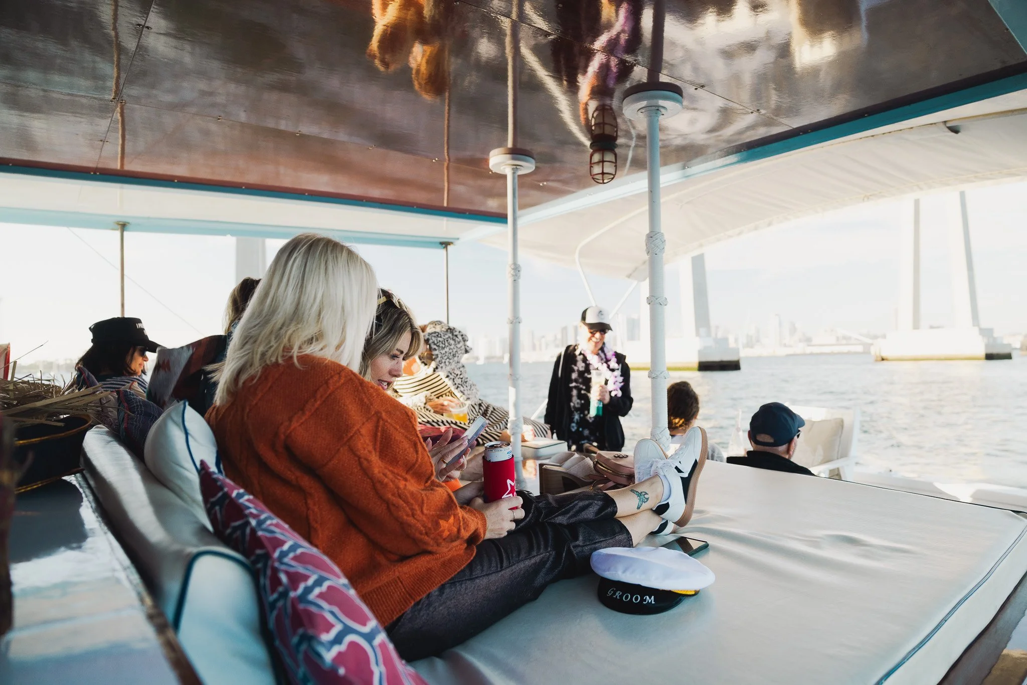 People sitting on a boat deck with a city skyline and a bridge in the background during daylight.