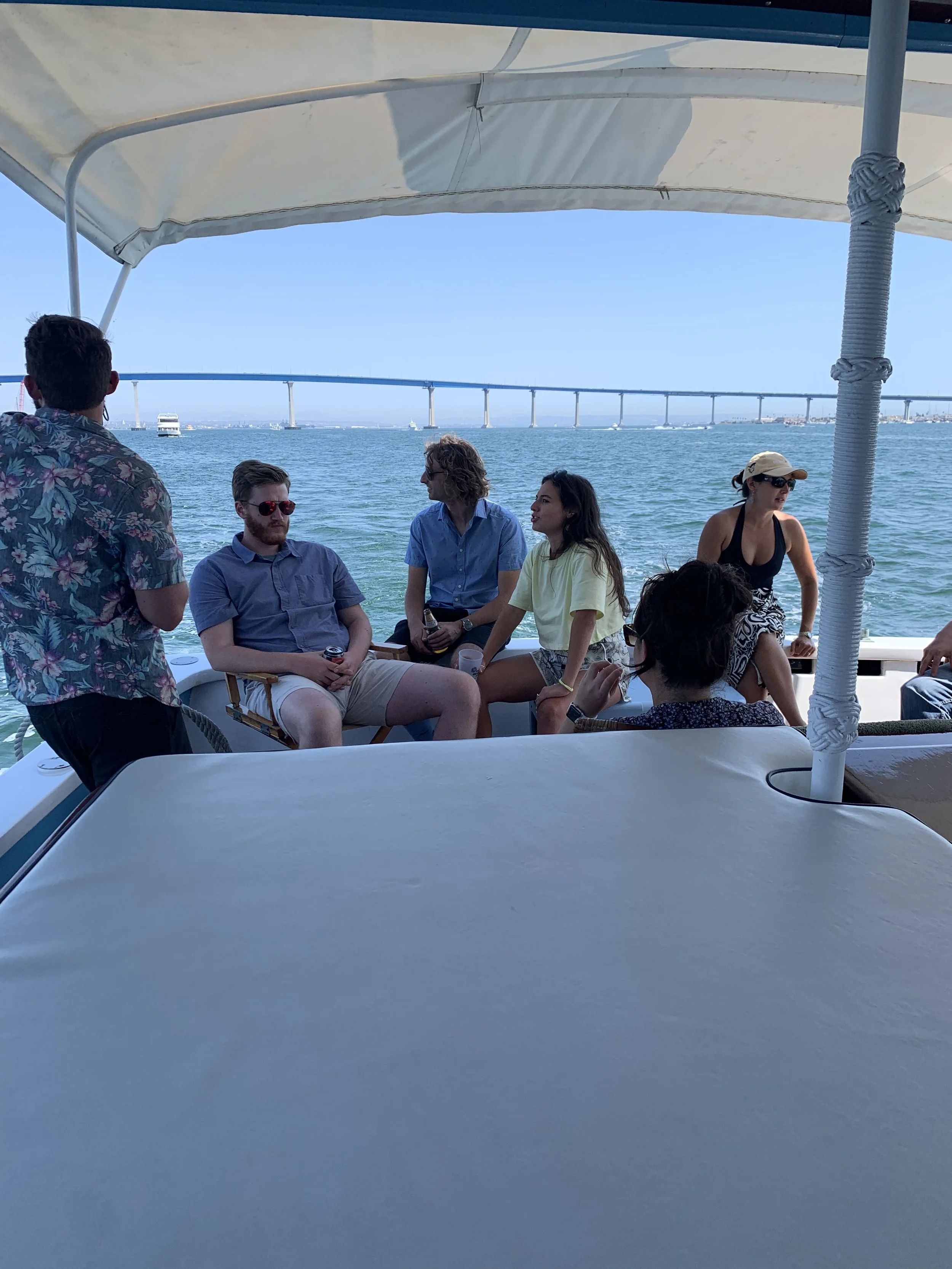People enjoying a boat ride on a sunny day, with a bridge stretching across the water in the background.