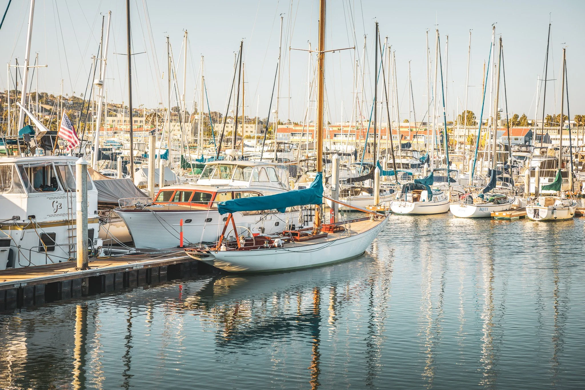 A marina with multiple sailboats and yachts docked, featuring a small boat with a brown wooden deck in the foreground.