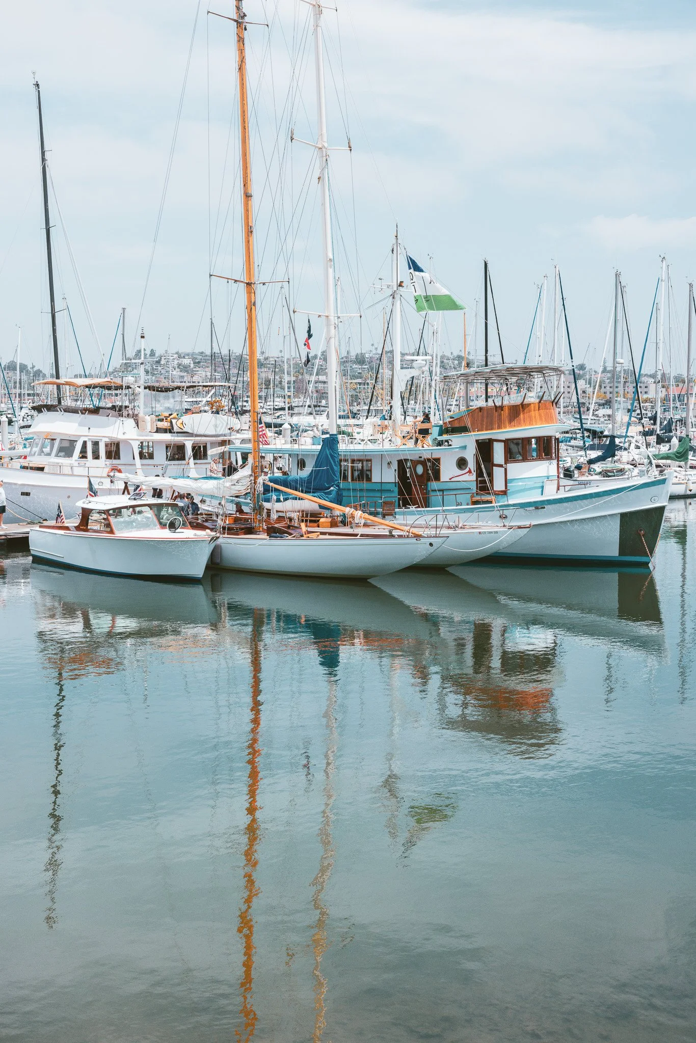 Boats docked at a marina, with reflections in the water, under a cloudy sky.