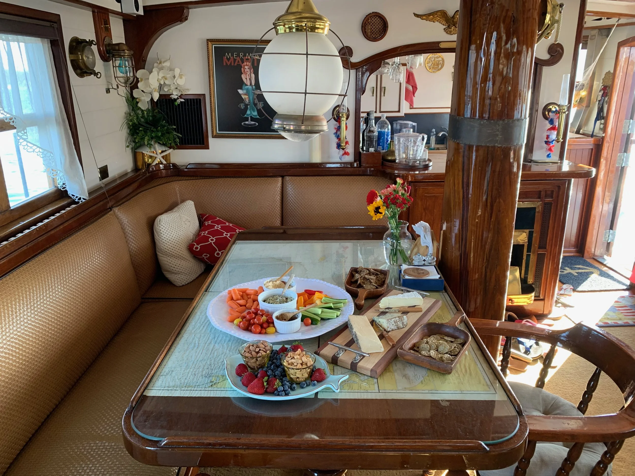 A dining table with cheese, crackers, vegetables, fruits, and dips in a cozy, well-decorated room with wooden furniture and artwork on the wall.