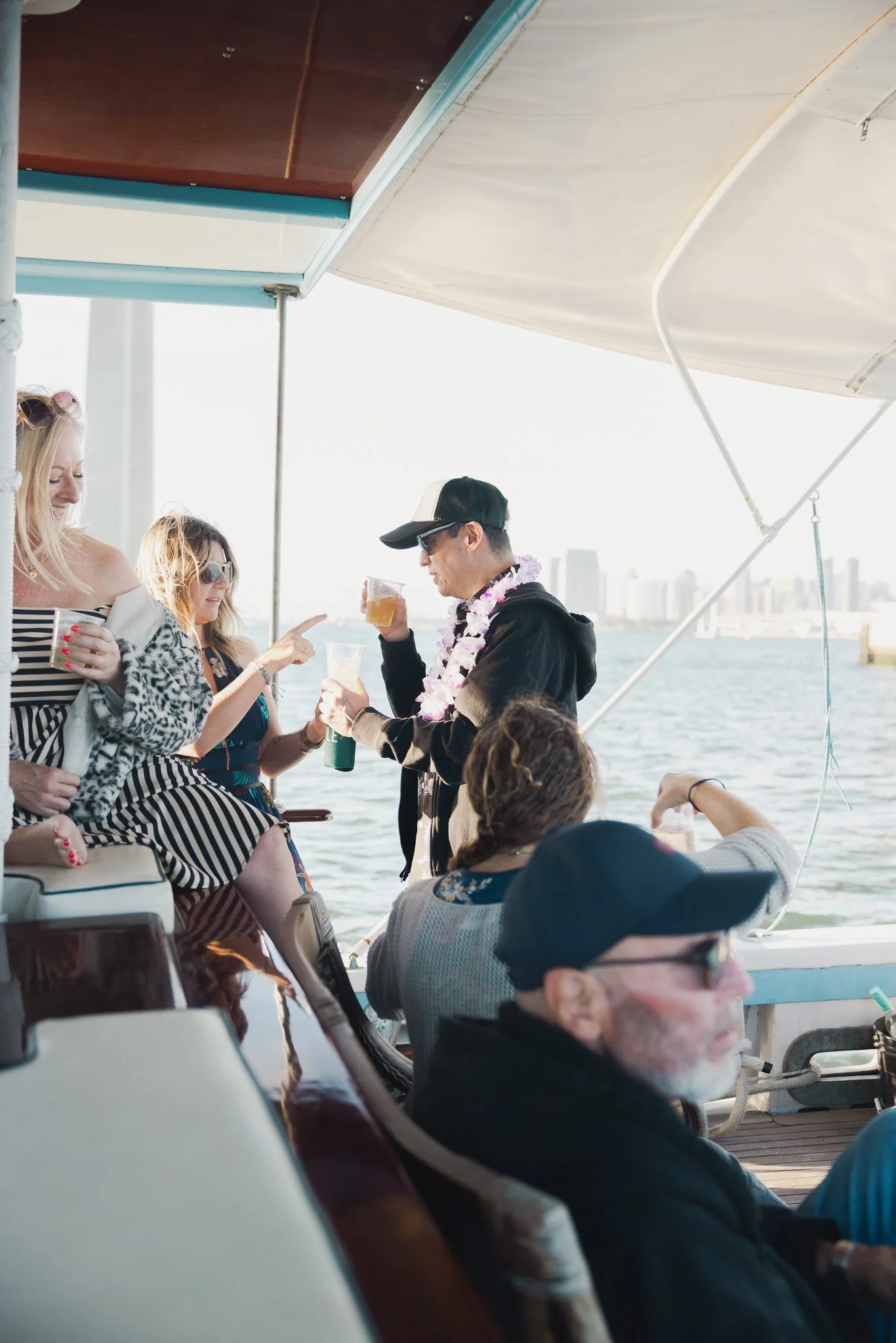 Group of friends enjoying drinks on a boat with a city skyline in the background.