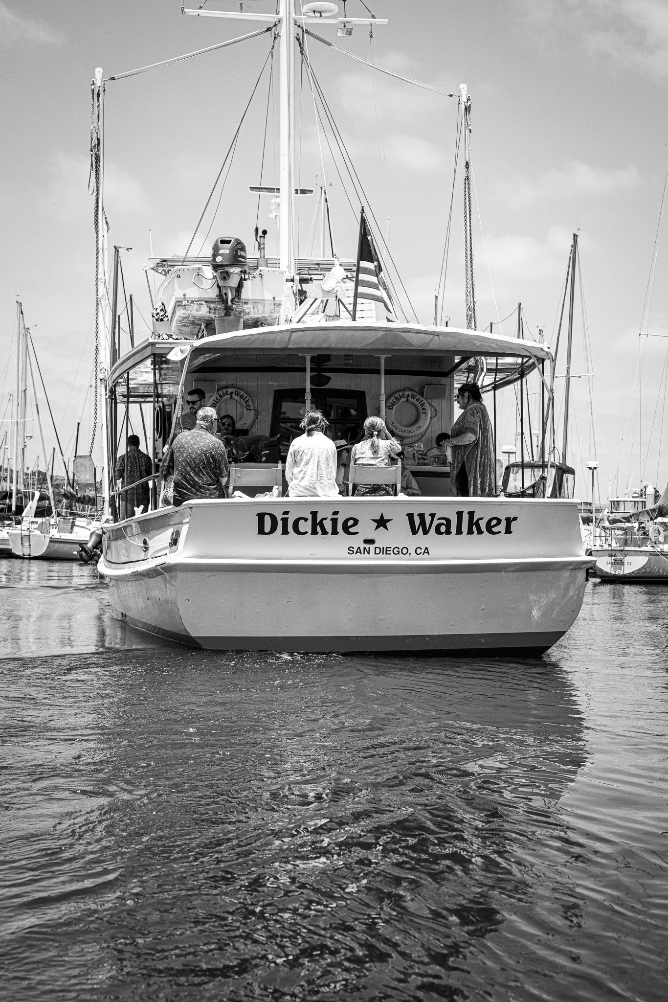 People disembarking from a boat docked at a wooden pier, with some on the boat and one woman on the gangway, engaging with the crew at the entrance.