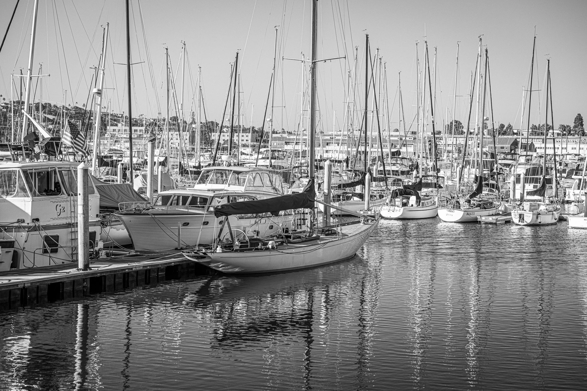 Black and white photo of boats docked at a marina, with multiple sailboats and yachts moored at the pier.
