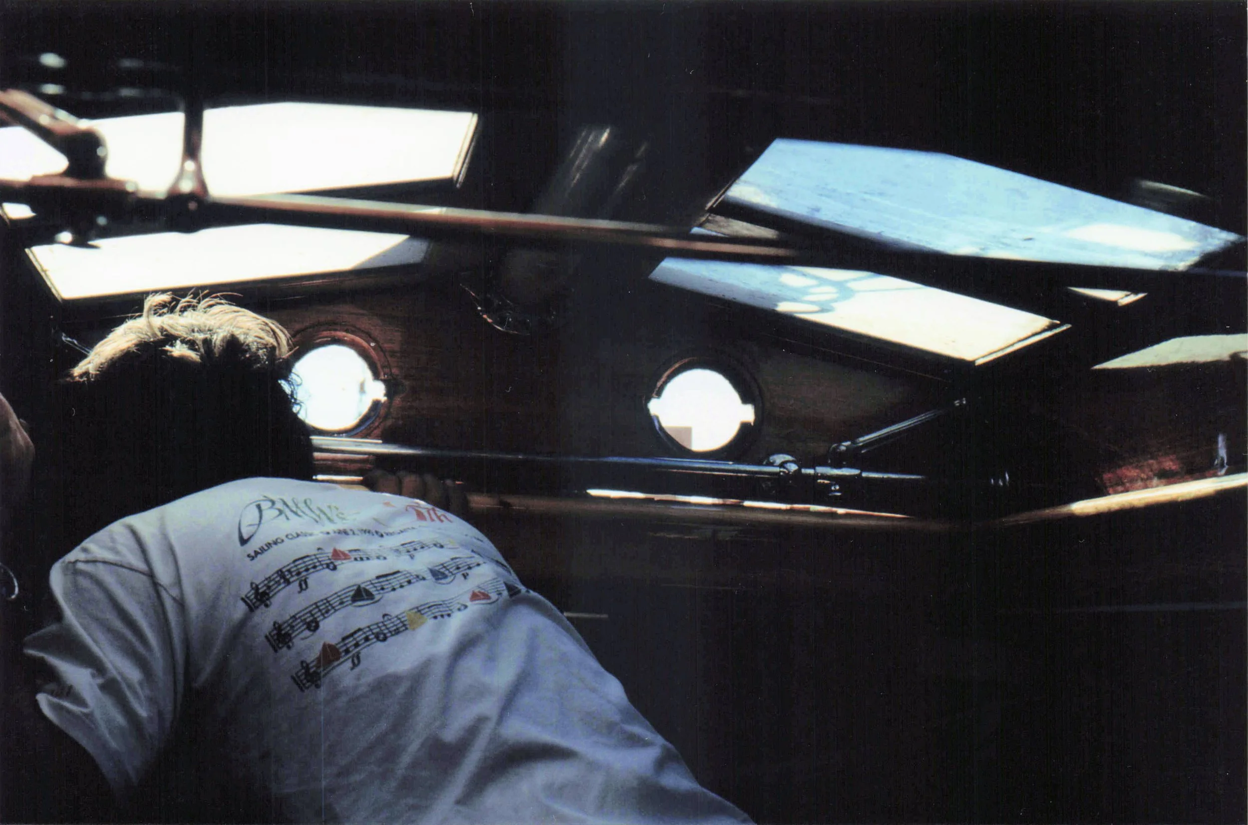 The interior view from a pilot's perspective inside an airplane cockpit, showing the helm, windows, and part of the pilot's white shirt with musical notes and text.