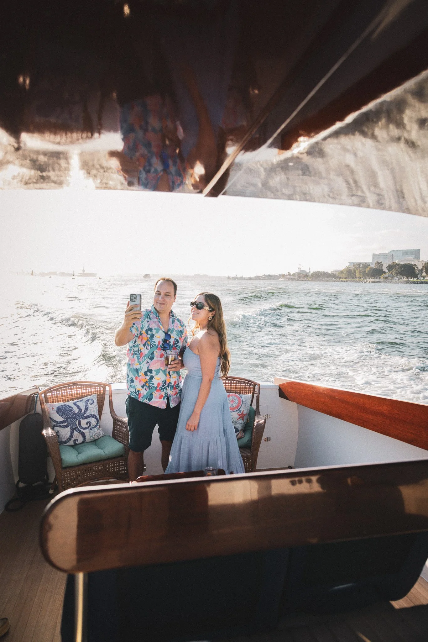 A couple taking a selfie on a boat with a water view in the background during sunset.