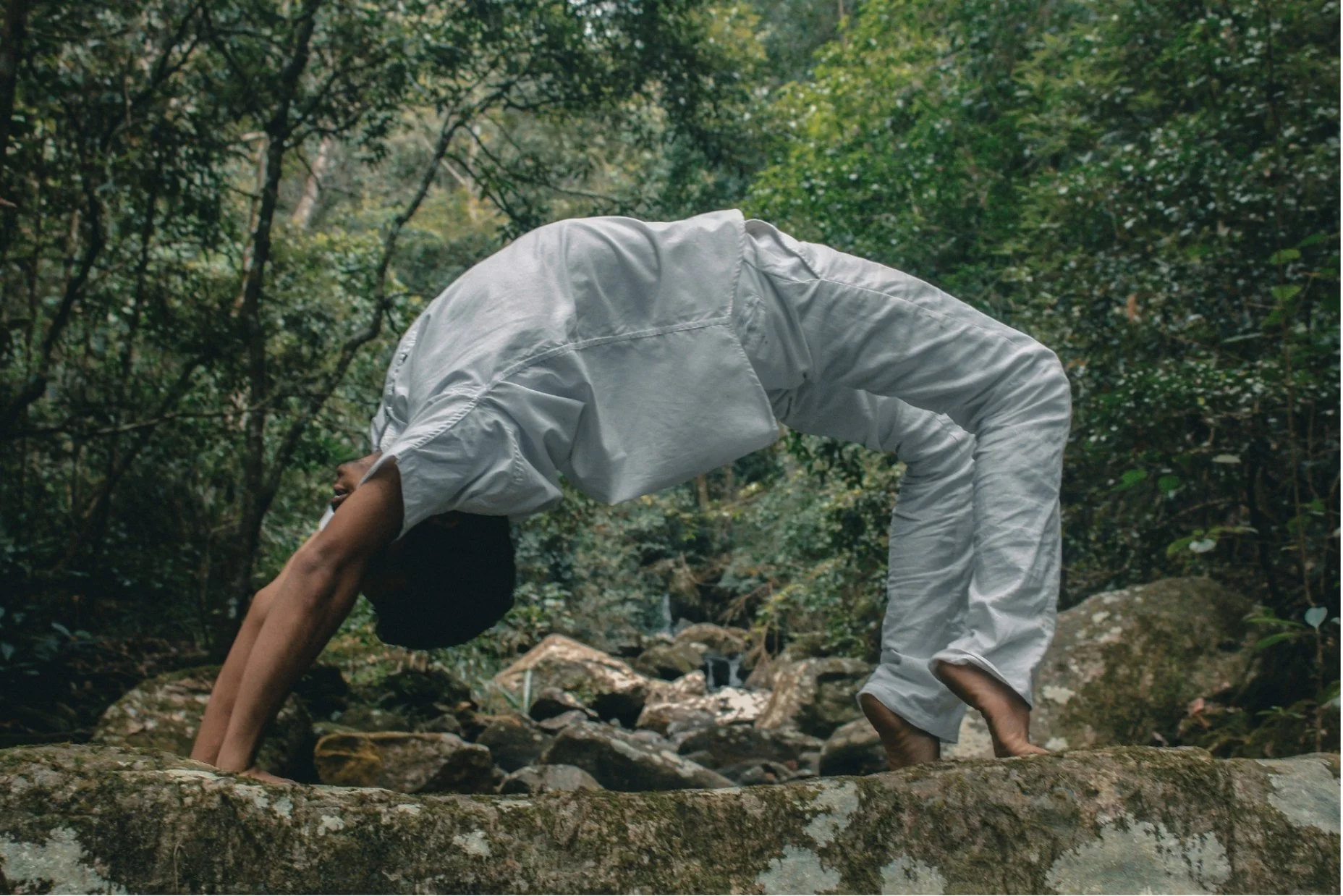 Person practicing Hatha Yoga in a natural outdoor setting near Setúbal, Portugal – gentle backbend pose surrounded by trees and rocks.