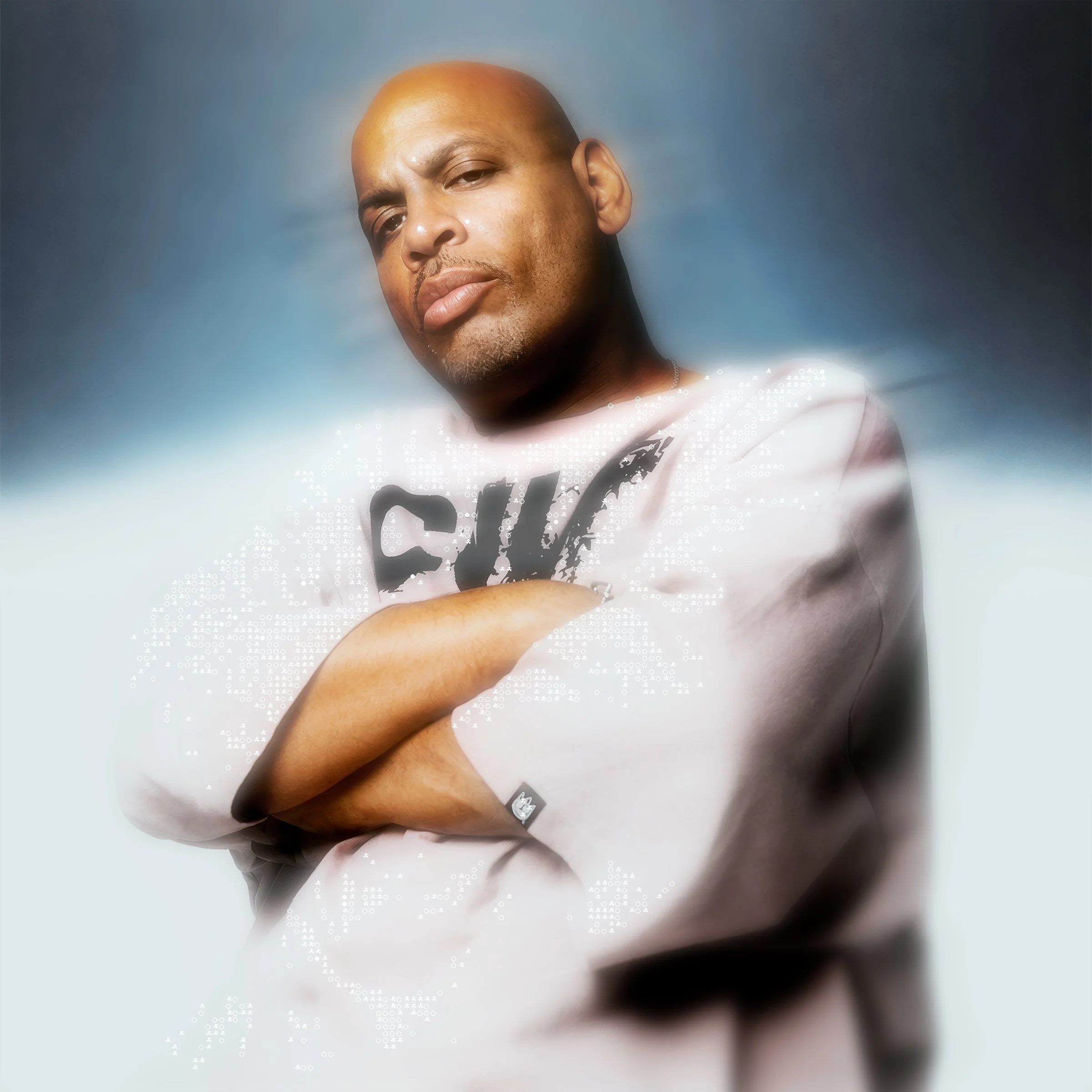 Close-up of a man with a shaved head looking at the camera, wearing a white shirt with a graphic print, against a blue gradient background.