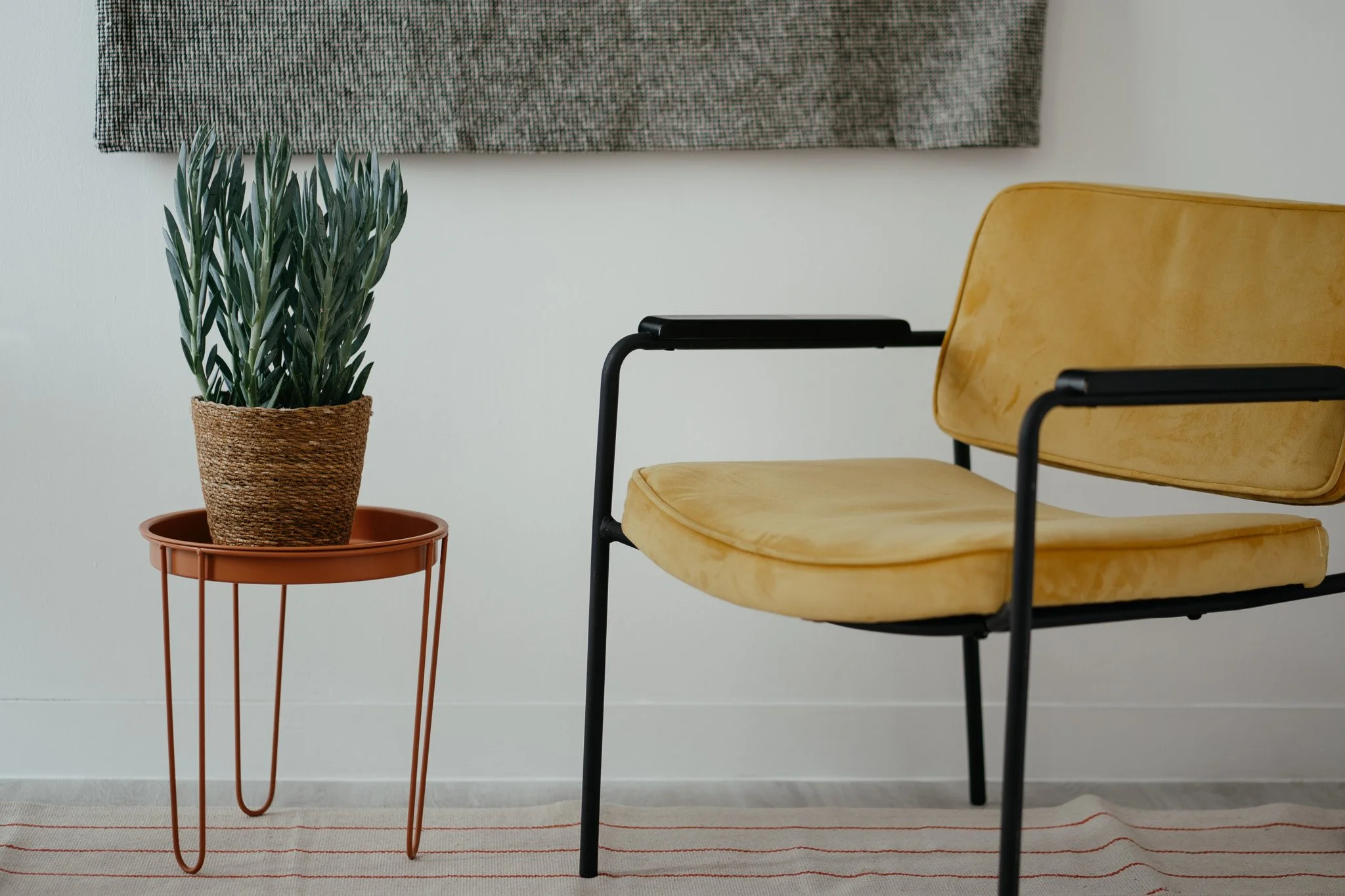 A modern wooden house with large glass windows is set against a mountainous landscape with dry grass and small trees in the foreground.