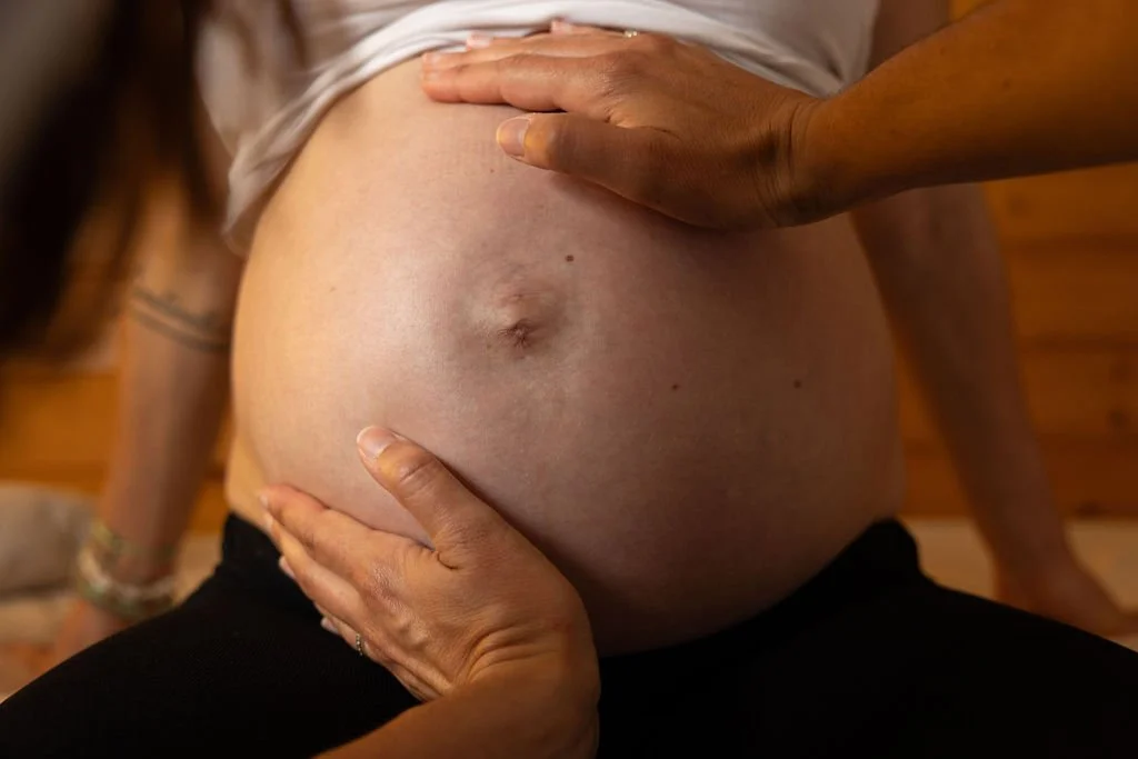 Une femme enceinte avec une main posée sur son ventre rond et une autre main soutenant son ventre.