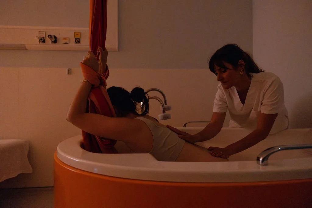 Une femme recevant une séance de bain moussant avec une professionnelle dans une salle de bain d'hôpital ou de maternité.