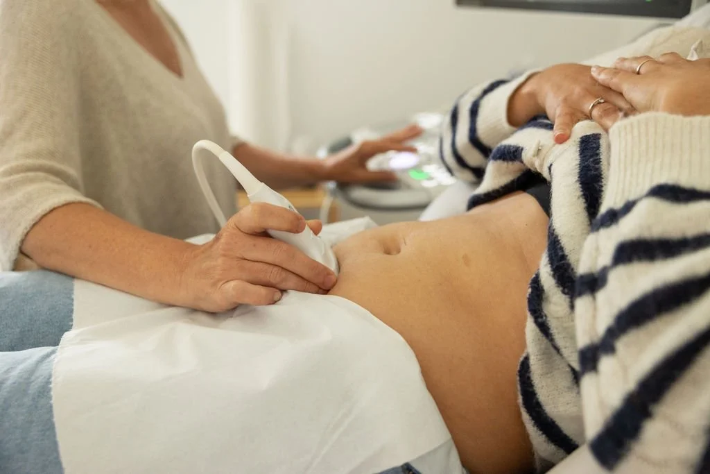 Une femme réalise une échographie abdominale sur une autre personne allongée sur un lit.