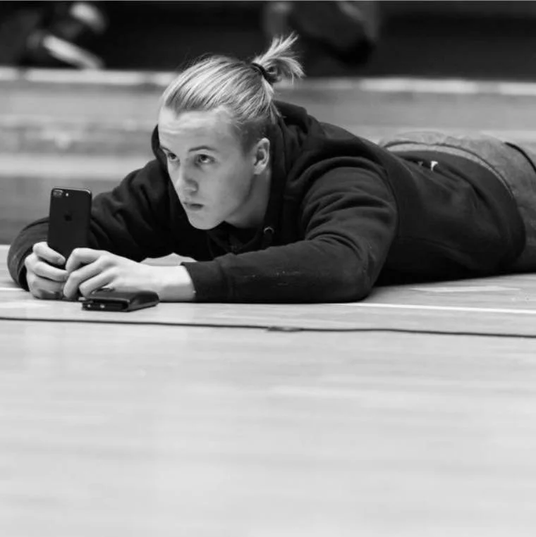 Person lying on their stomach on the floor, holding a smartphone, with a focused expression.