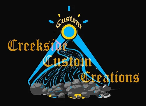 Logo with a black background featuring a stylized blue water stream flowing through a grafitti style showerhead, surrounded by rocks. The words 'Creekside Custom Creations' are written in gothic font overlaying the design.