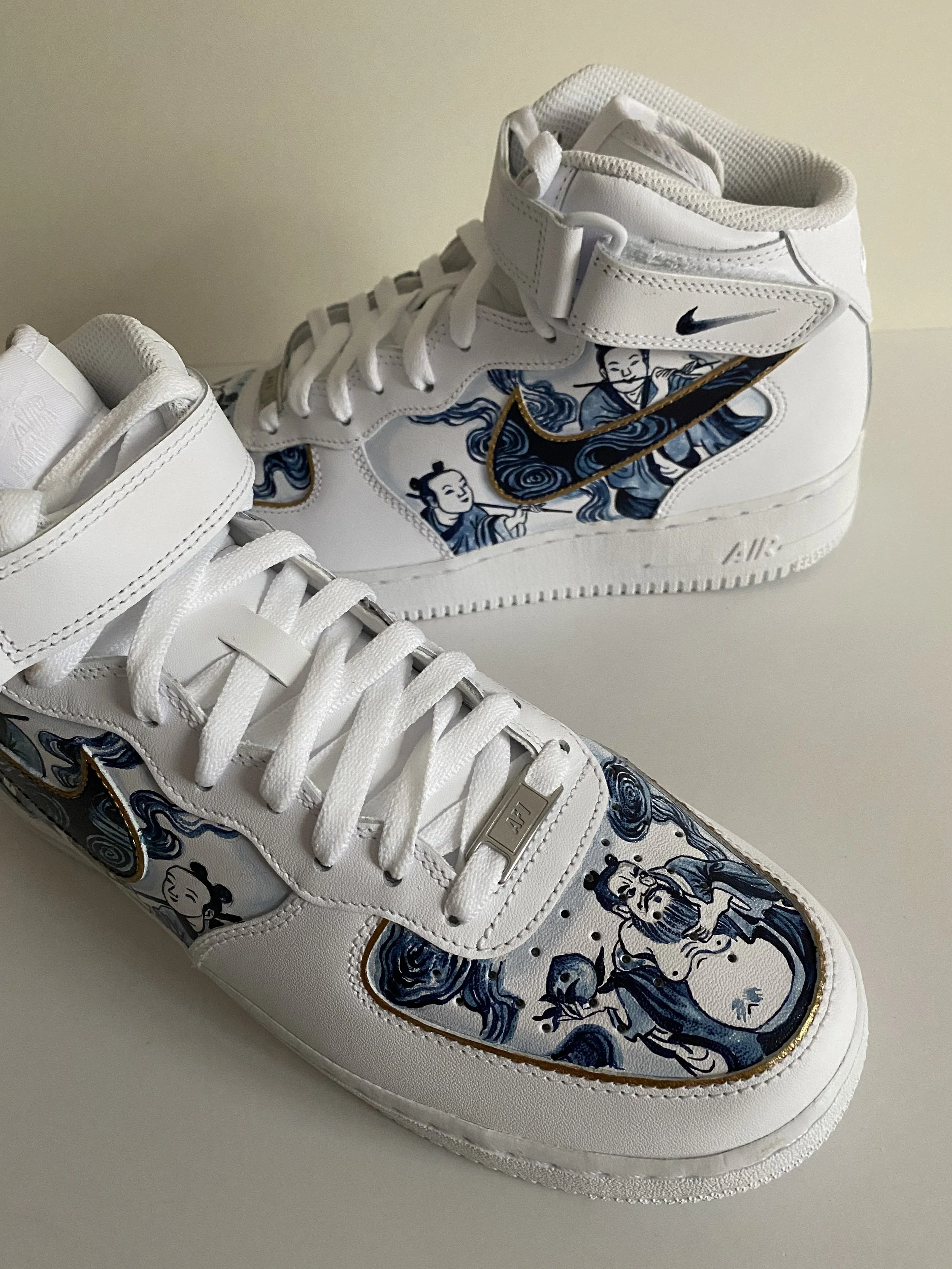 Custom white sneakers with blue and black artwork featuring Asian-style characters and motifs, gold accents, and Nike branding.