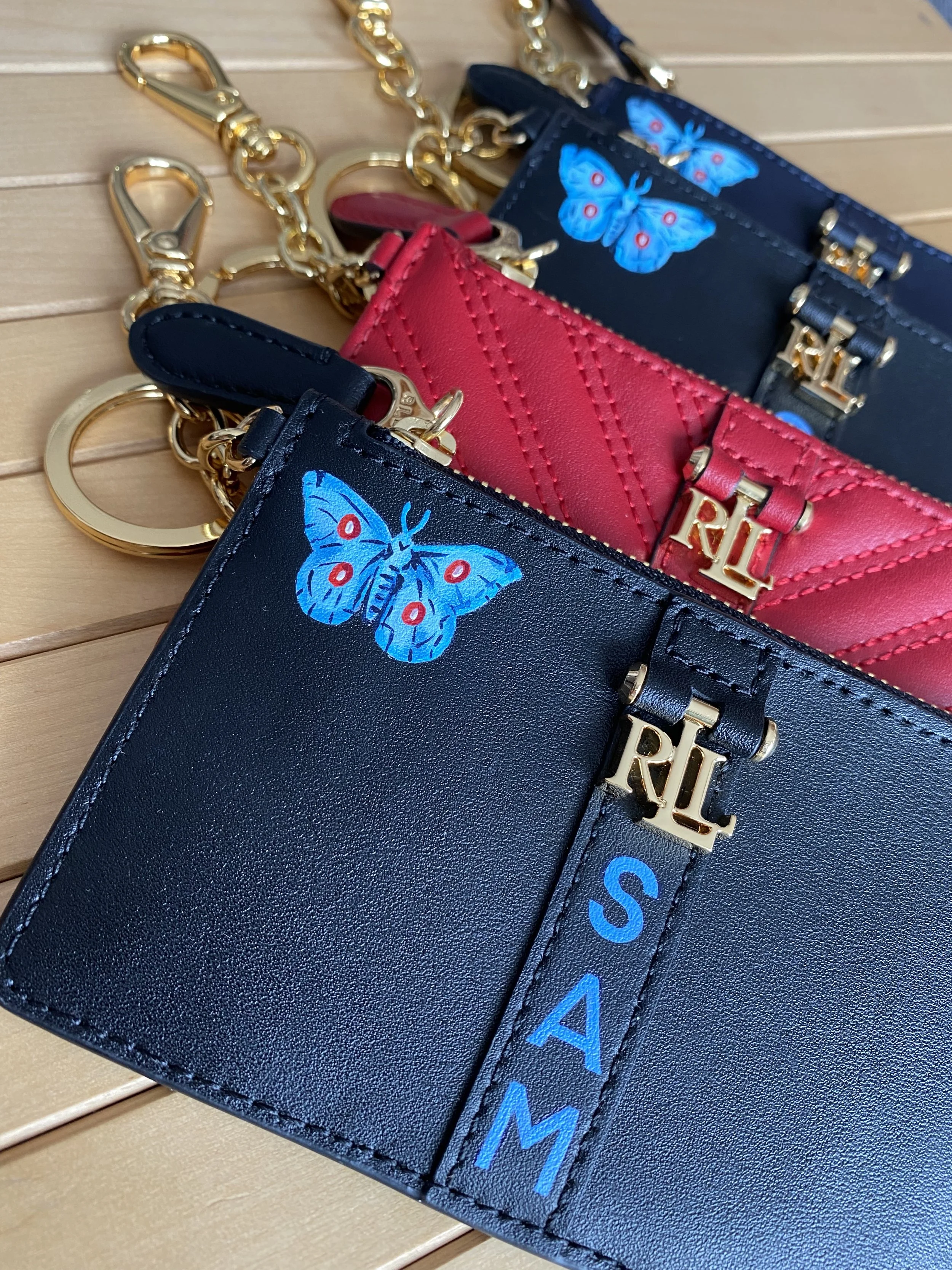 Close-up of three designer cardholders with butterfly motifs and gold-tone hardware, placed on a wooden surface.
