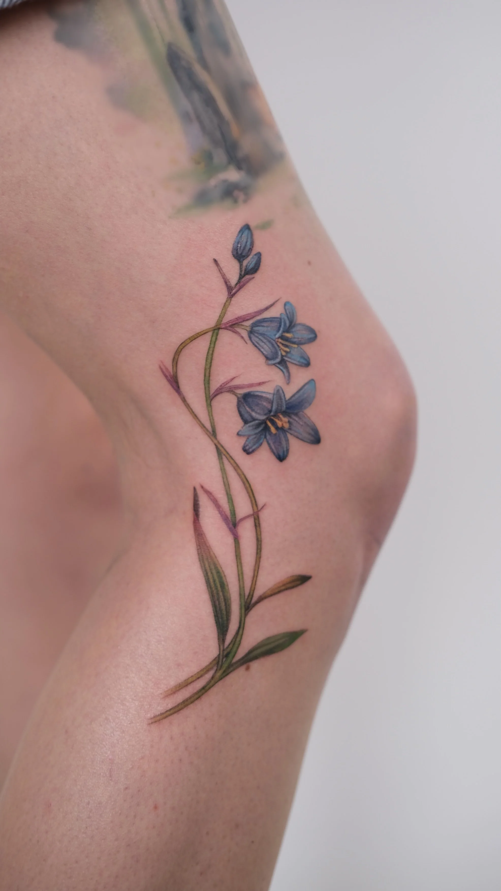 Close-up of a colorful tattoo of blue flowers on the person's knee.