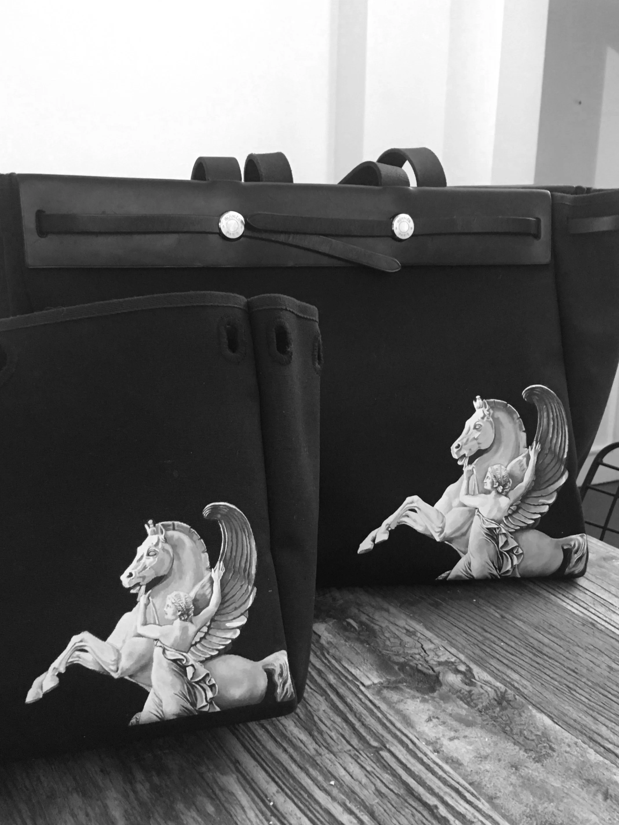Two black bags with a horse and angel graphic sitting on a wooden surface.